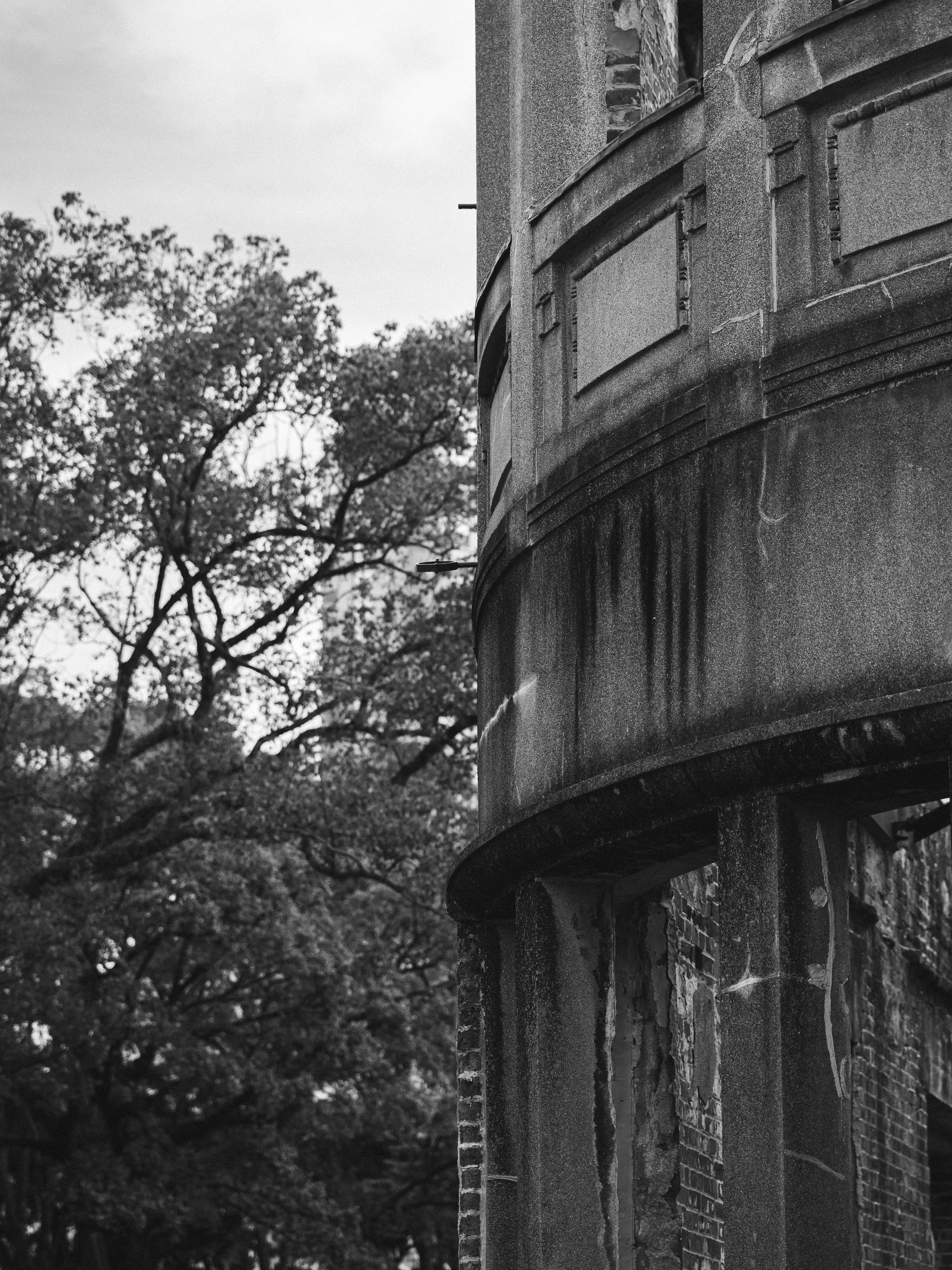 The curved façade of the Atomic Bomb Dome, its weathered concrete layers peeling beside autumn foliage.