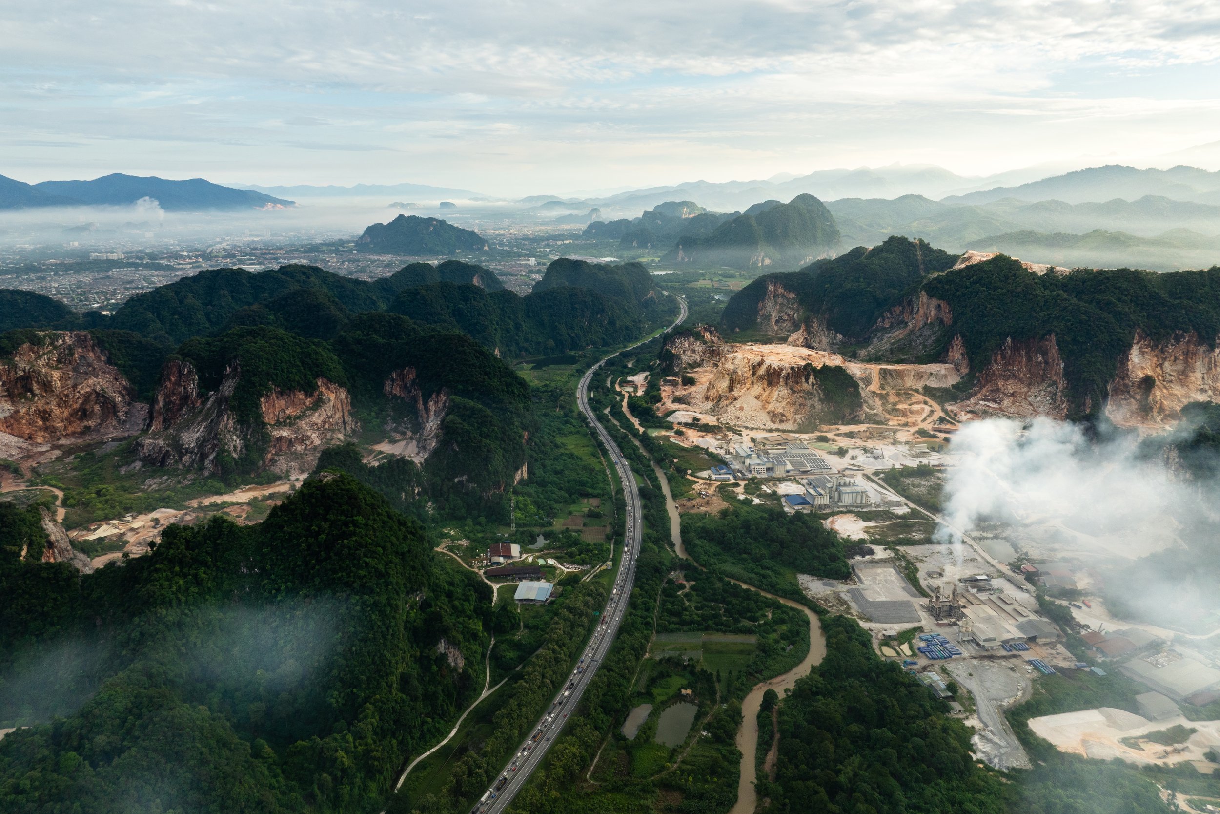 Aerial view of a highway cutting through limestone karst hills and active quarry operations in Simpang Pulai, Ipoh, Perak.