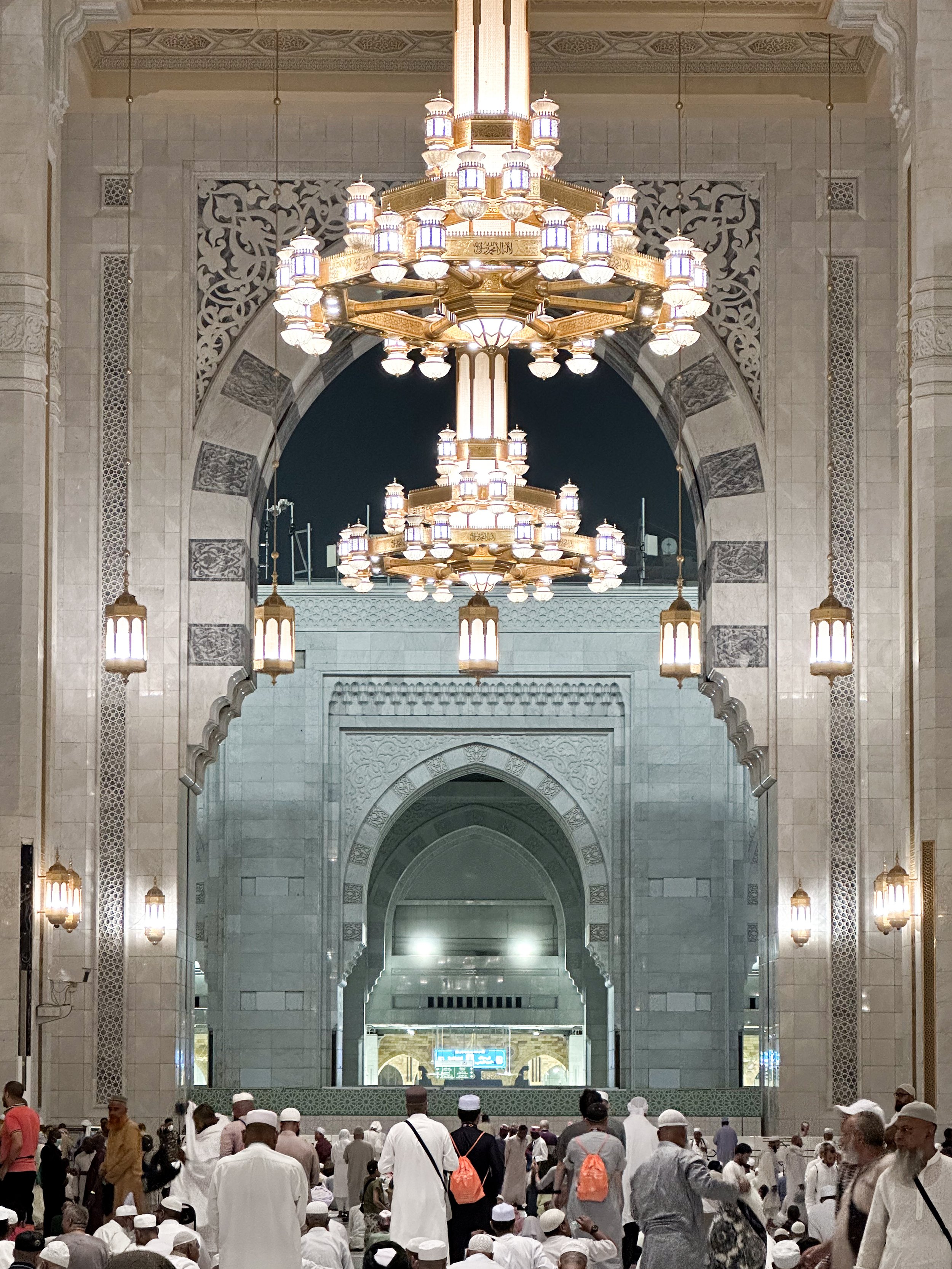 Masjidil Haram, Mecca, Saudi Arabia — Pilgrims move through the grand interior of the Haram at night, gold chandeliers glowing beneath carved arches that stretch deeper than the eye can follow. The mosque never fully sleeps.