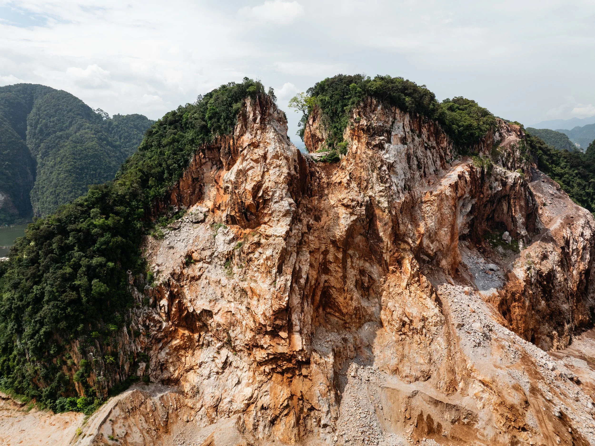 Close aerial view of a stripped limestone cliff face in Perak, where quarrying has exposed raw rock beneath the remaining forest canopy.