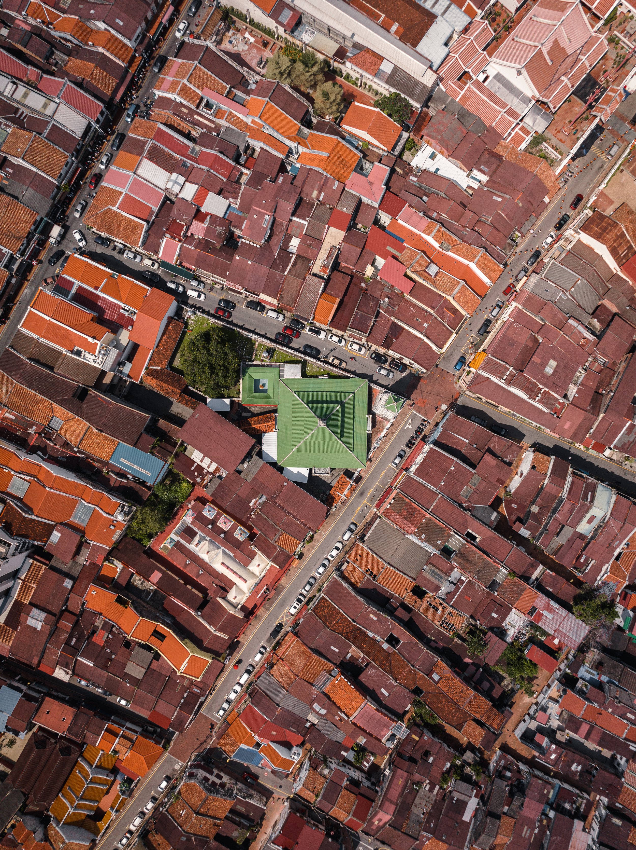 Bandar Hilir, Melaka, Malaysia — Directly above the heritage quarter, terracotta rooftops fill every inch of the frame. A single, green-roofed mosque holds its ground at the centre, surrounded by a century of shophouses. Order hiding inside the densi