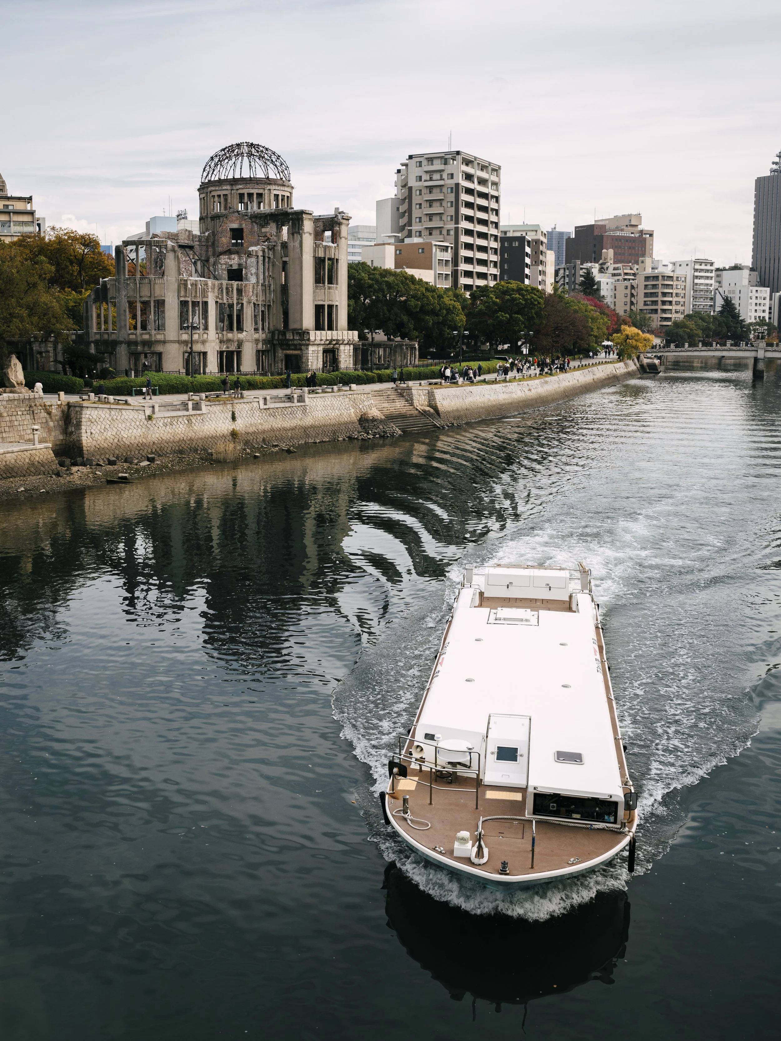 A river cruise boat passes the Atomic Bomb Dome along the Motoyasu River, with Hiroshima's modern skyline behind.