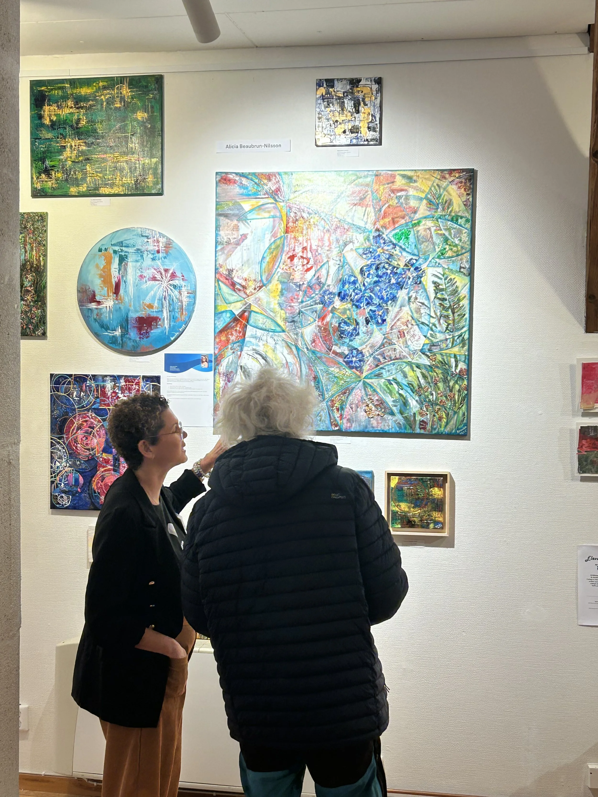 Two people are looking at colourful abstract paintings in an art gallery.