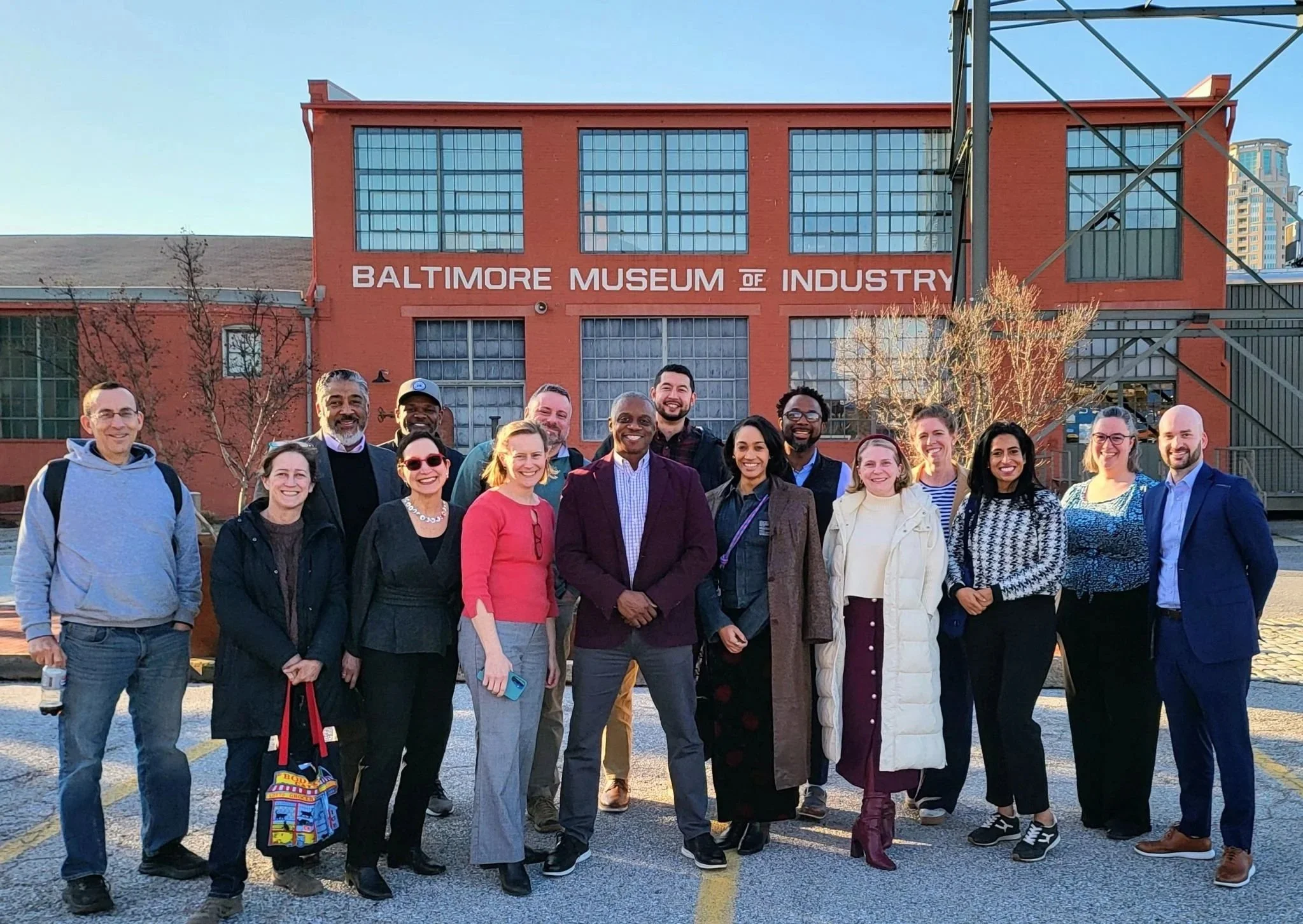 A group of diverse people standing outside in front of the Baltimore Museum of Industry, smiling for the photo.
