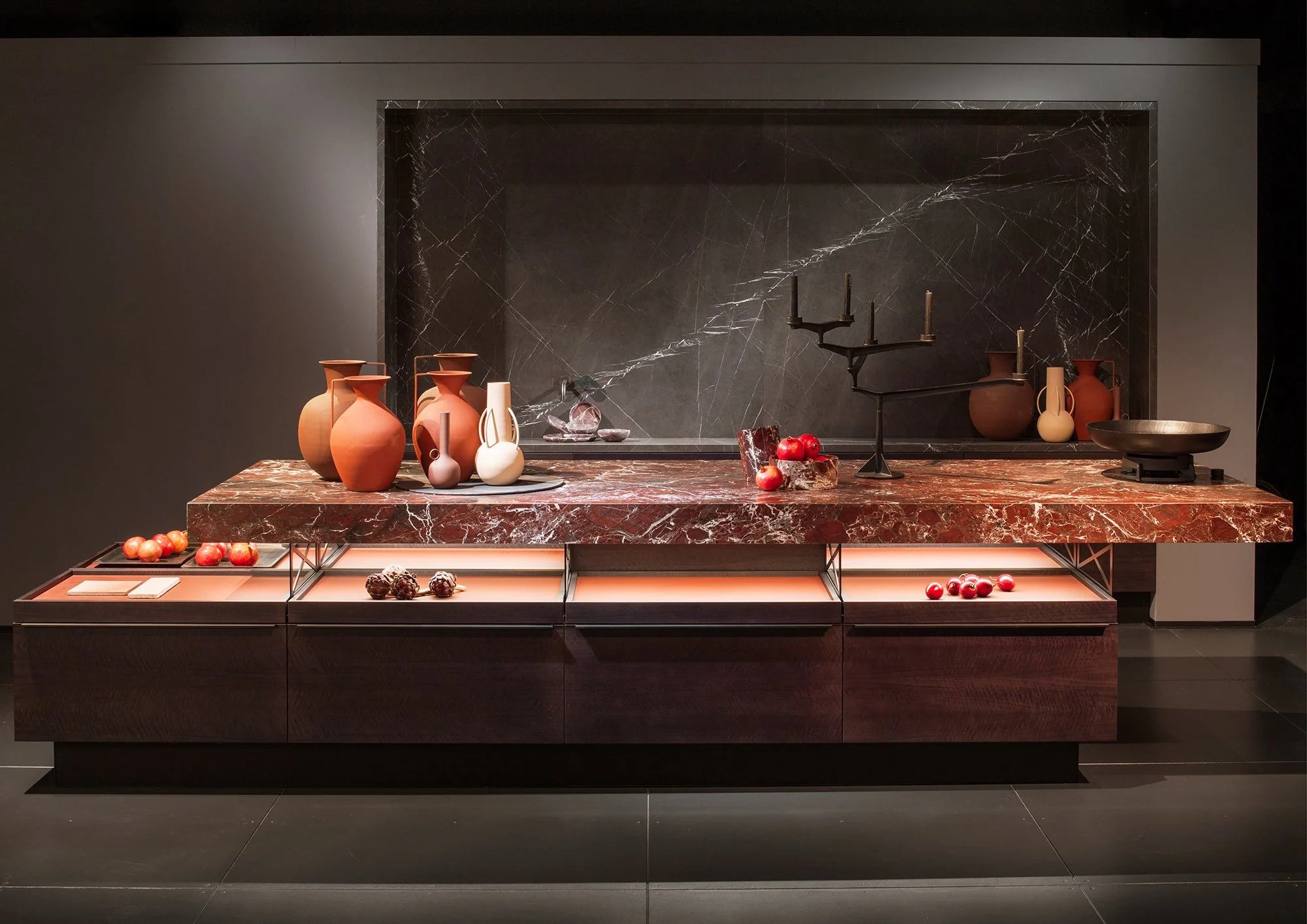Display of vases, apples, and decor on a red marble counter with a dark marble accent wall.