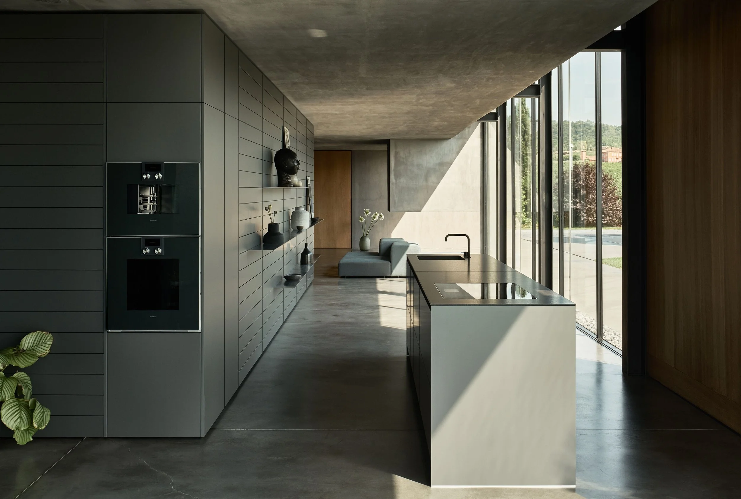 Modern kitchen interior with large floor-to-ceiling windows, gray cabinetry, a marble countertop, and decorative vases and art on the wall.