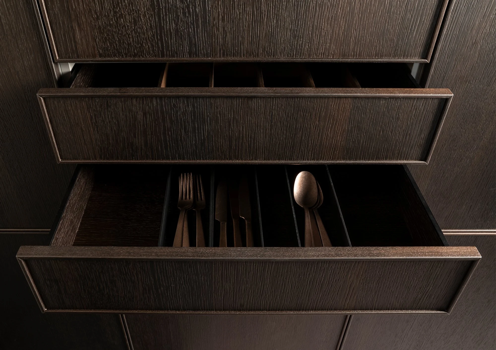 A dark brown wooden drawer with utensils inside, partially pulled out.