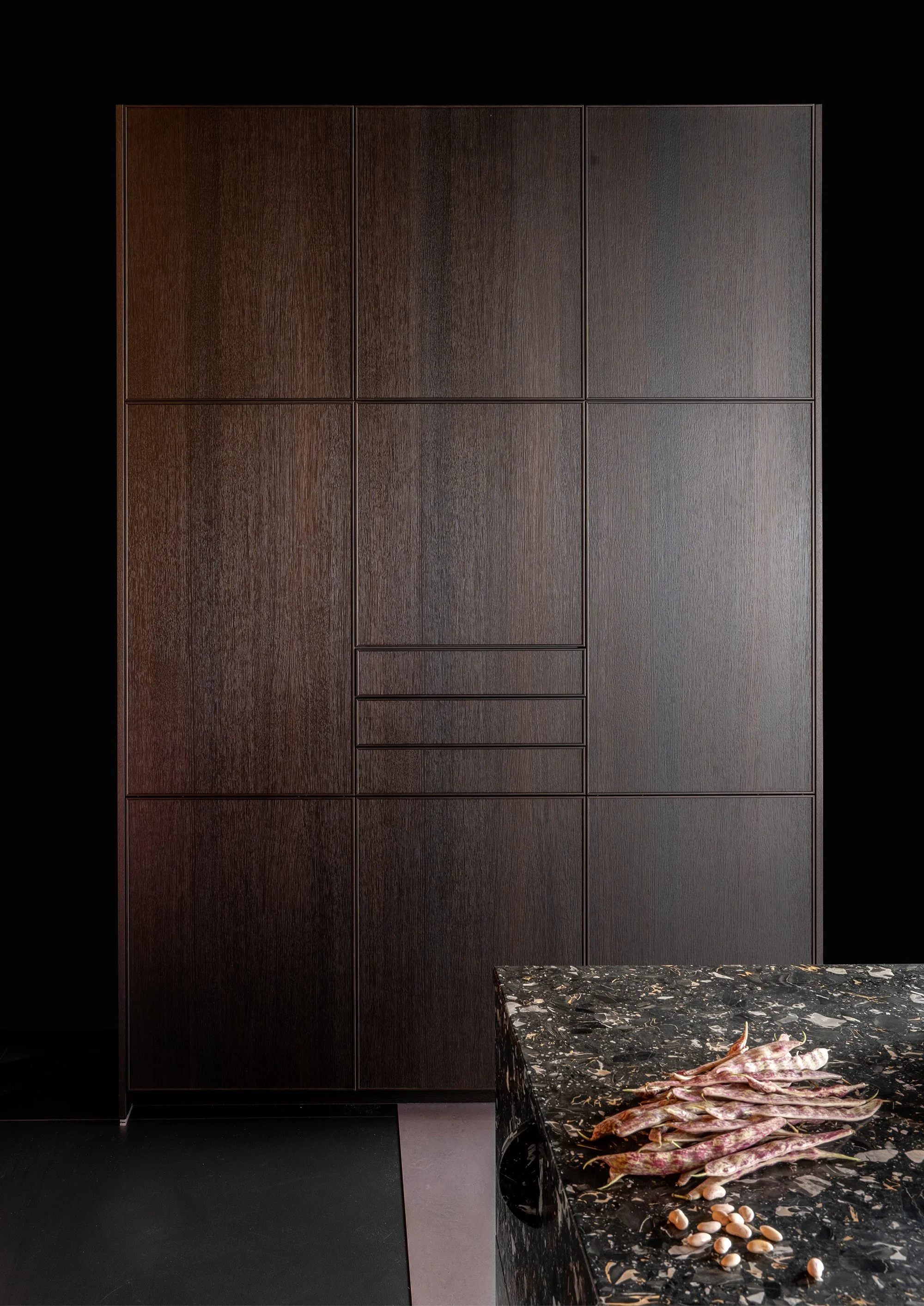 Dark wooden cabinets against a black wall and a black marble countertop with raw meat and seafood.