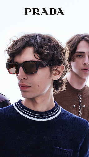 Close-up of two young models, one wearing Prada sunglasses and a navy sweater with white stripes, the other with long hair and a chain necklace.