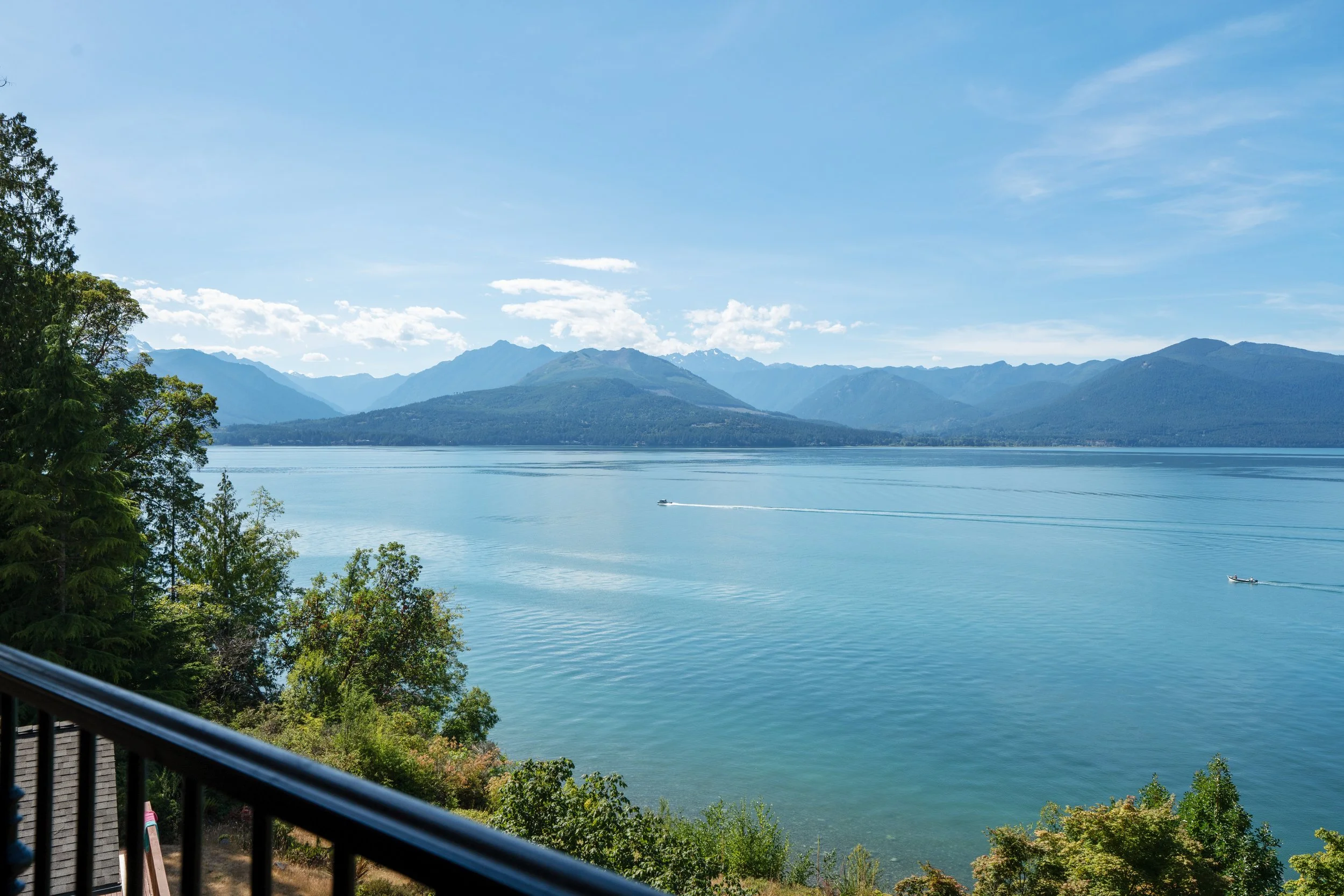 Scenic view of a large body of water with mountains in the background, trees in the foreground, and a boat on the water.