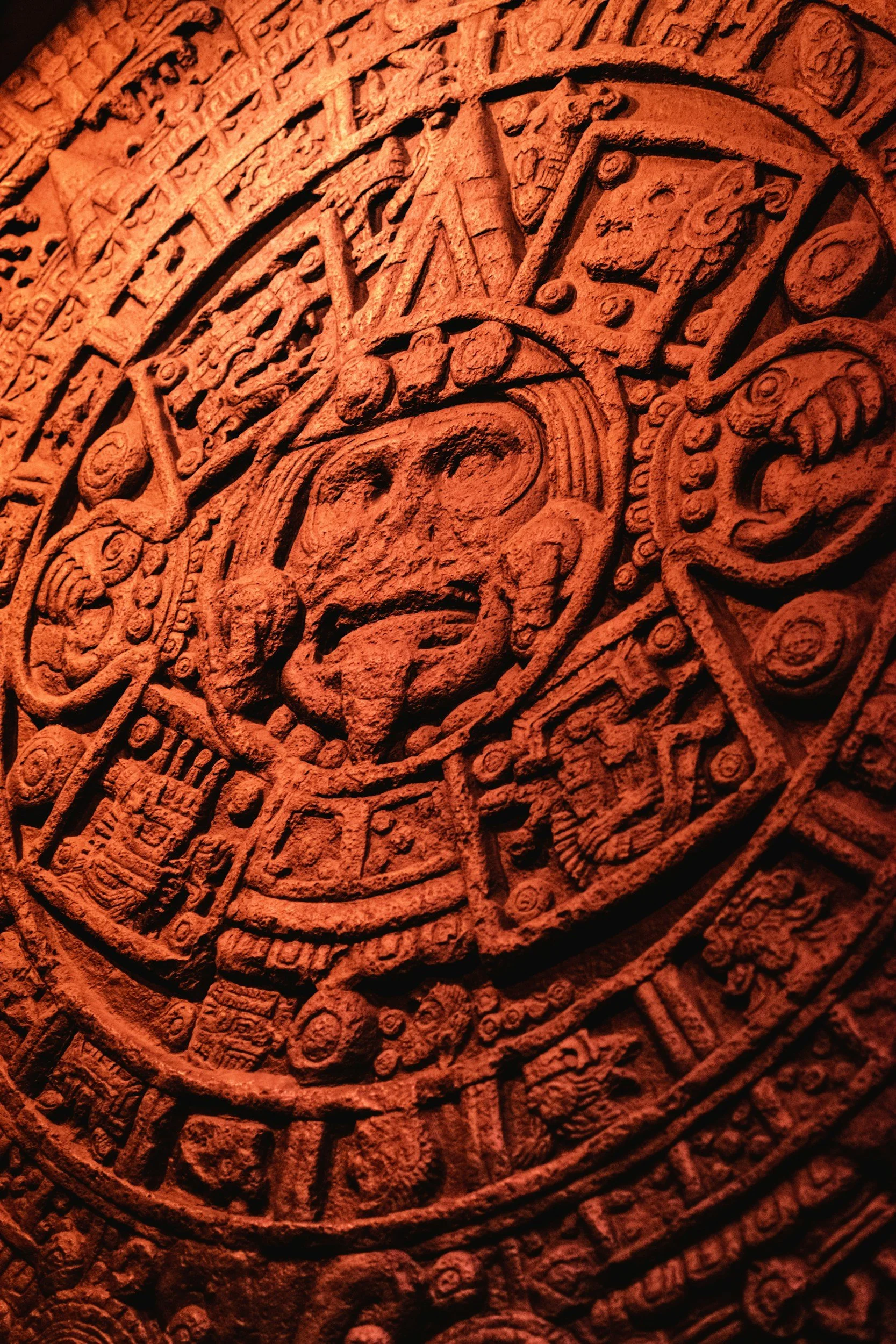 Close-up of an ancient circular stone carving with detailed Aztec or Mayan glyphs and symbols in reddish-brown color.