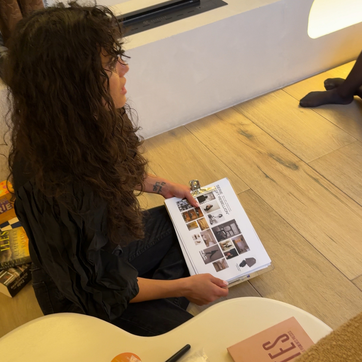 Una mujer con cabello rizado y oscuro, sentada en el suelo, mirando el moodboard de una sesion de fotos