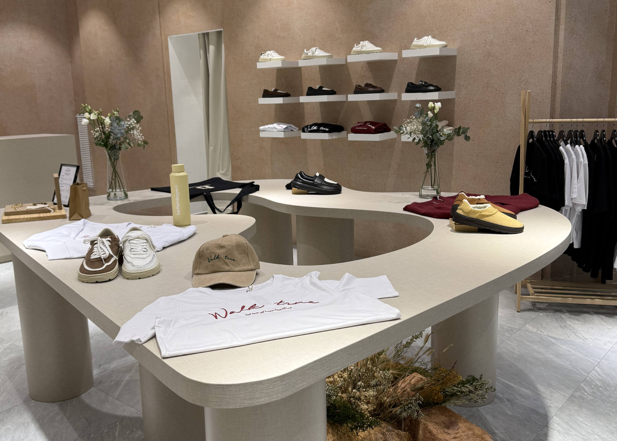 Mostrador de tienda con ropa, zapatos y accesorios, decorado con flores y plantas.