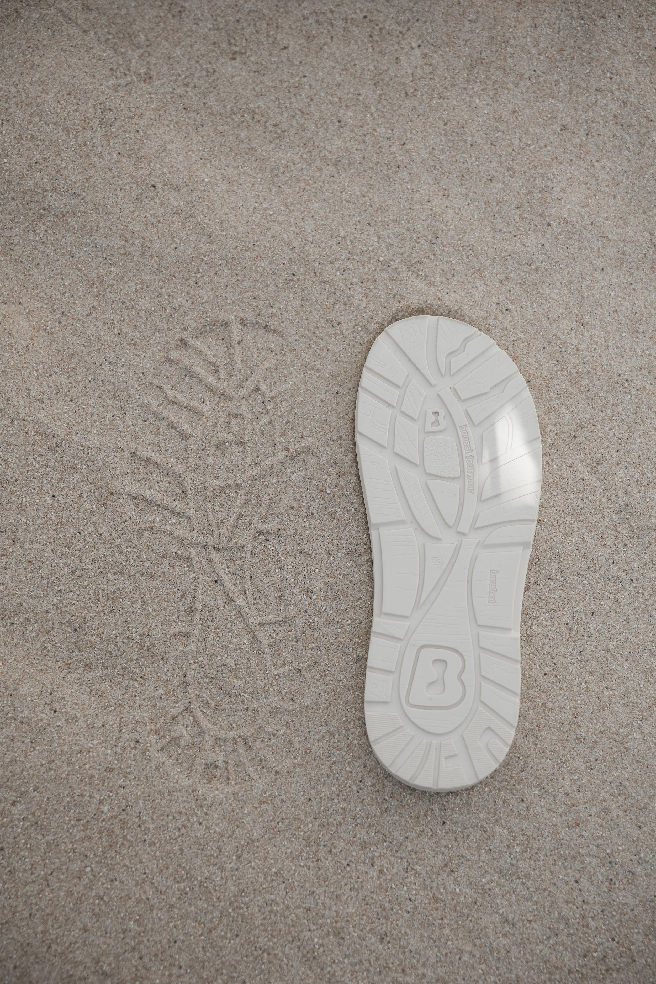 Sola blanca en la arena con marcas de pasos, vista de la plantilla de zapato