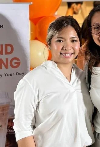 Aya Pajimola of Blackstem smiling at a brand event with orange balloons, featured in her client testimonial on the Huddle Design Studio homepage