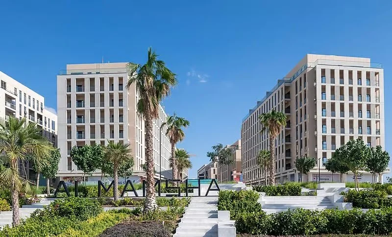 Modern high-rise buildings surrounded by palm trees and landscaped gardens under a clear blue sky.