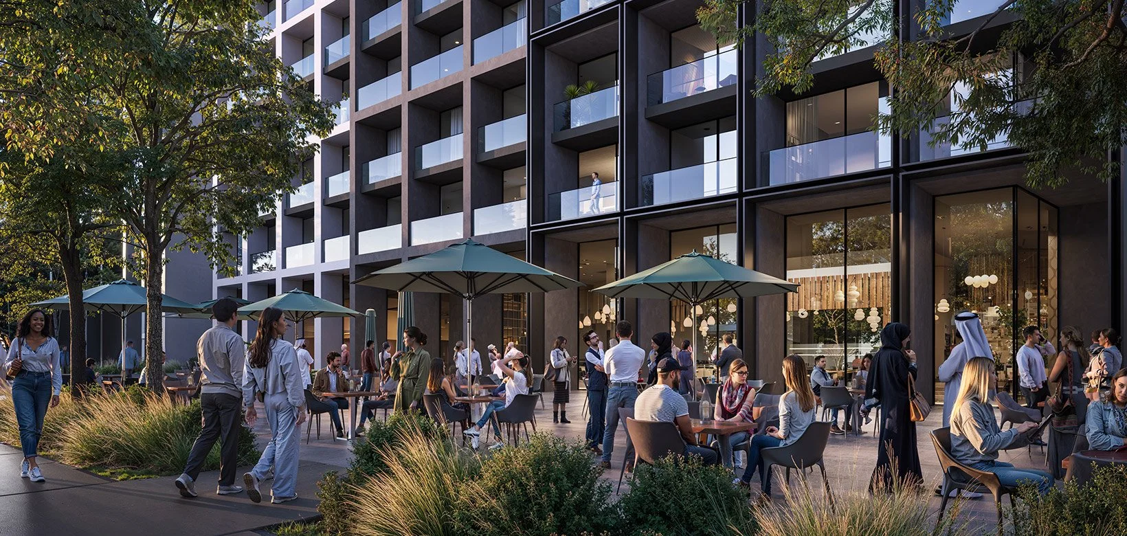 Outdoor patio area with people sitting and walking, surrounded by trees and plants, in front of a modern multi-story building with glass windows and balconies.