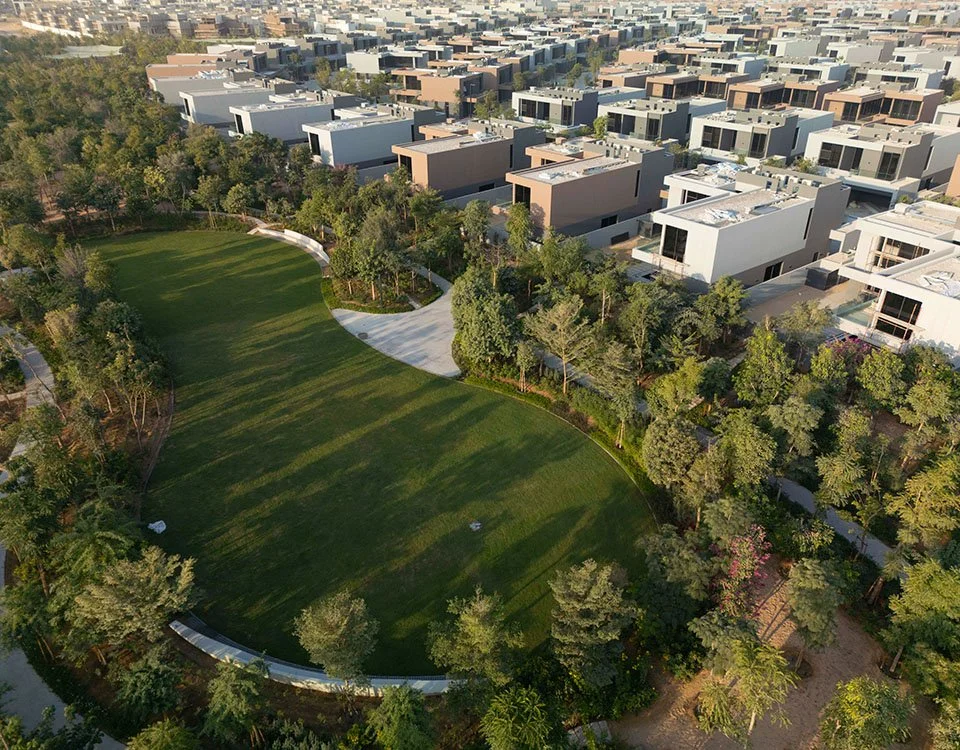 Aerial view of a residential neighborhood with modern white and gray homes and a large green park with trees.