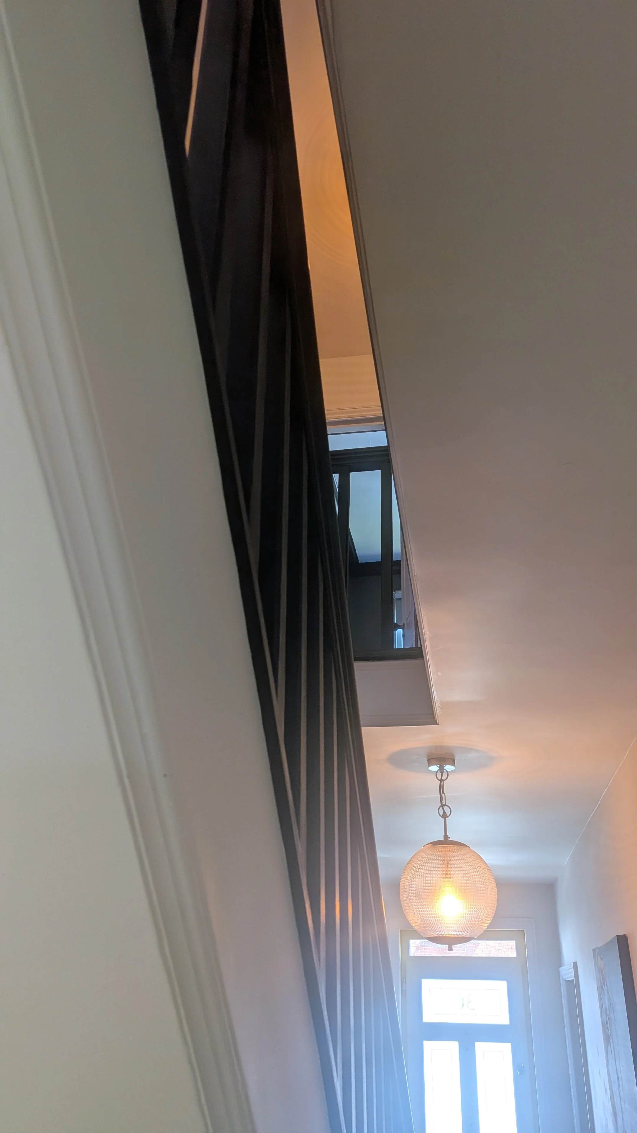 A hallway with a ceiling light fixture, a window, a door with glass panes, and a black curtain hanging from a rod.