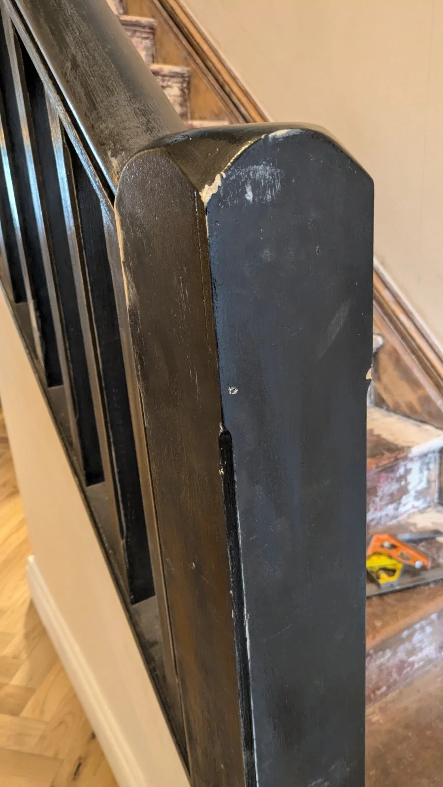 Close-up of a black wooden staircase railing with chipped paint, next to a wooden staircase with visible wear.