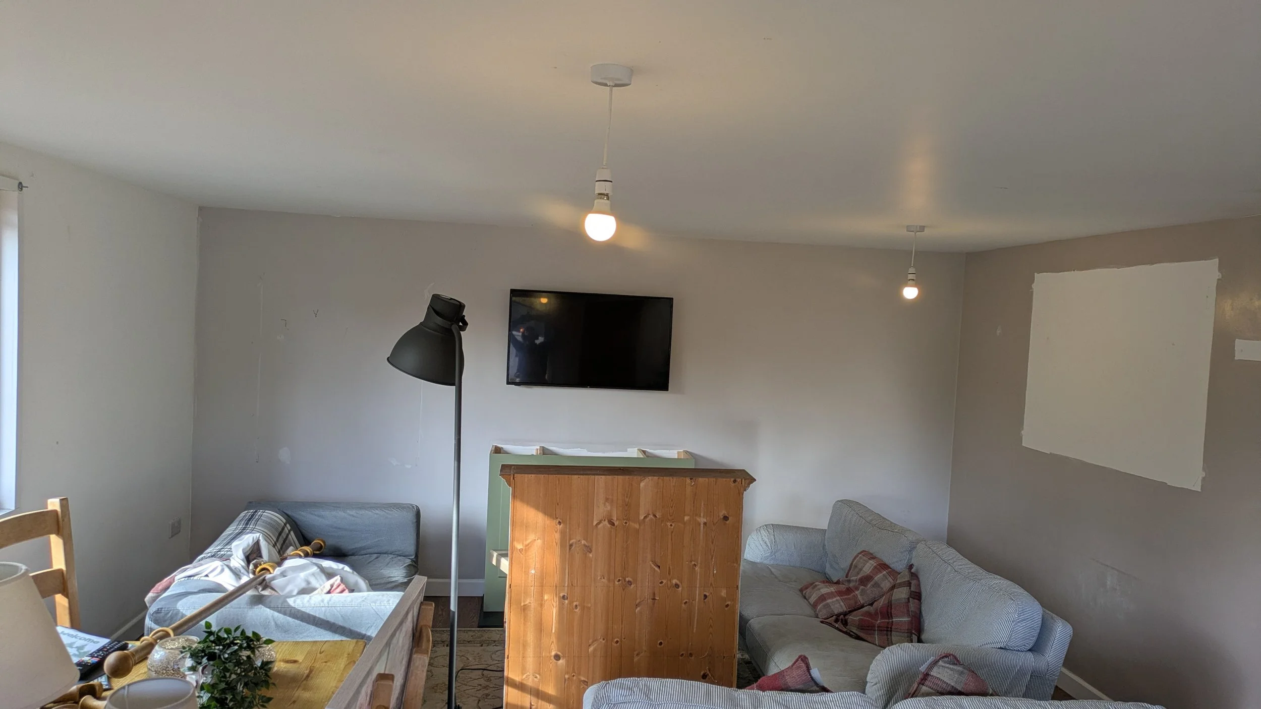 Living room with a gray couch, a wooden partition, a wall-mounted TV, a black floor lamp, lightbulb ceiling lights, and some furniture and objects in the room.
