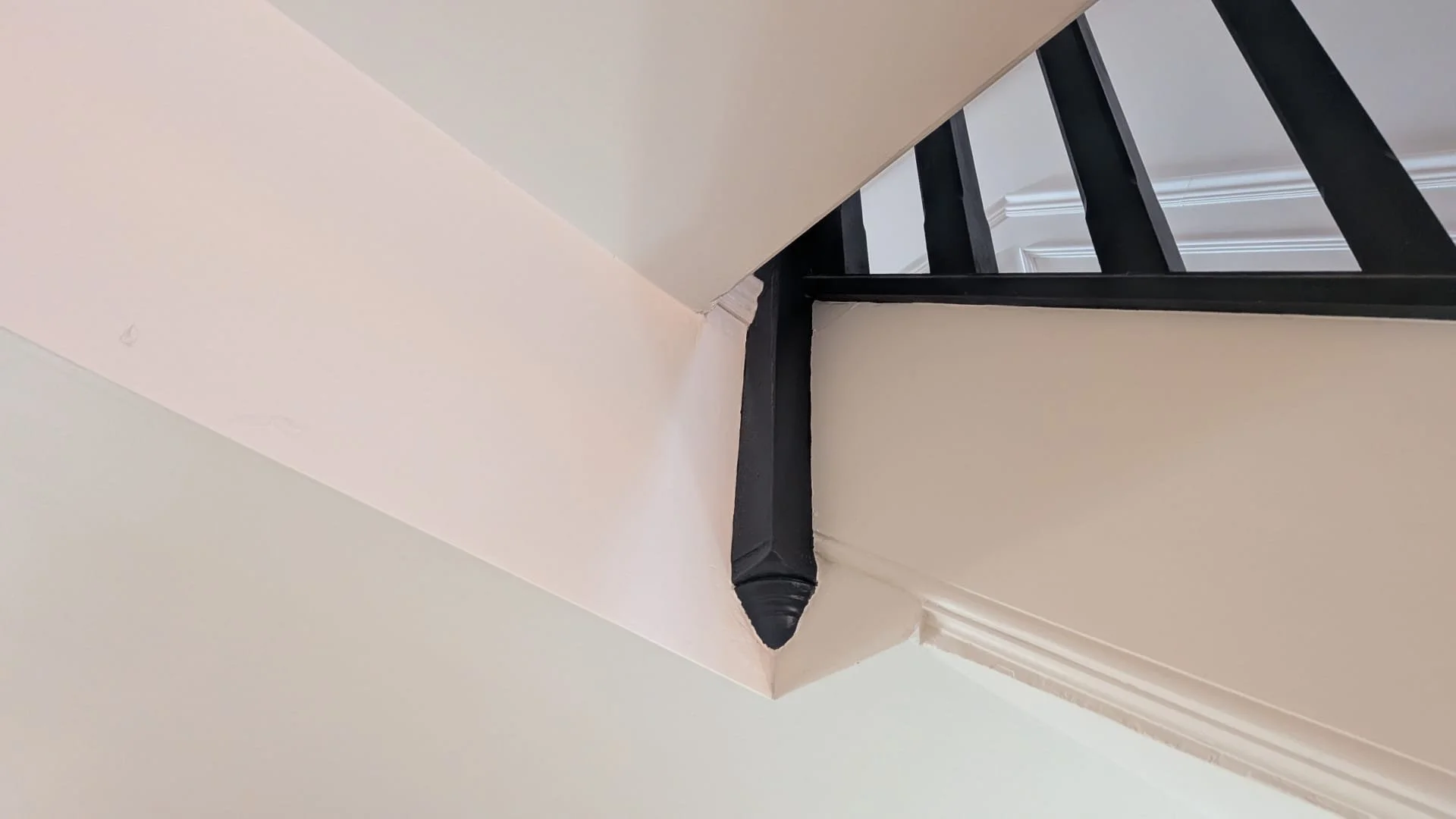 Upward view of a corner with a black pipe wrapped in insulation, a staircase with black spindles, and white decorative molding on the wall.