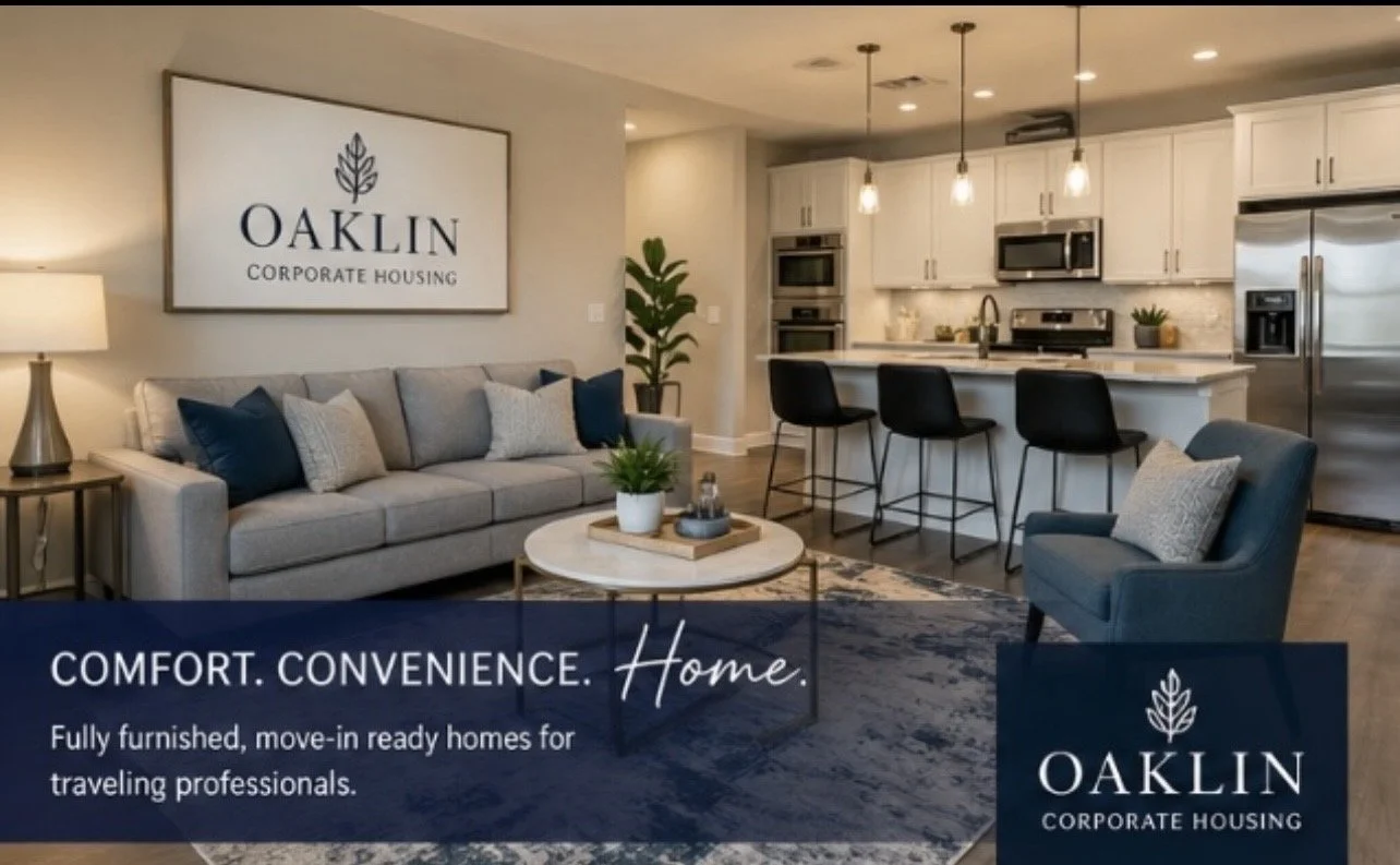 Interior of a fully furnished, move-in ready home with a living room and kitchen, featuring a gray couch, armchair, modern kitchen appliances, and a large sign that reads 'OAKLIN Corporate Housing.'