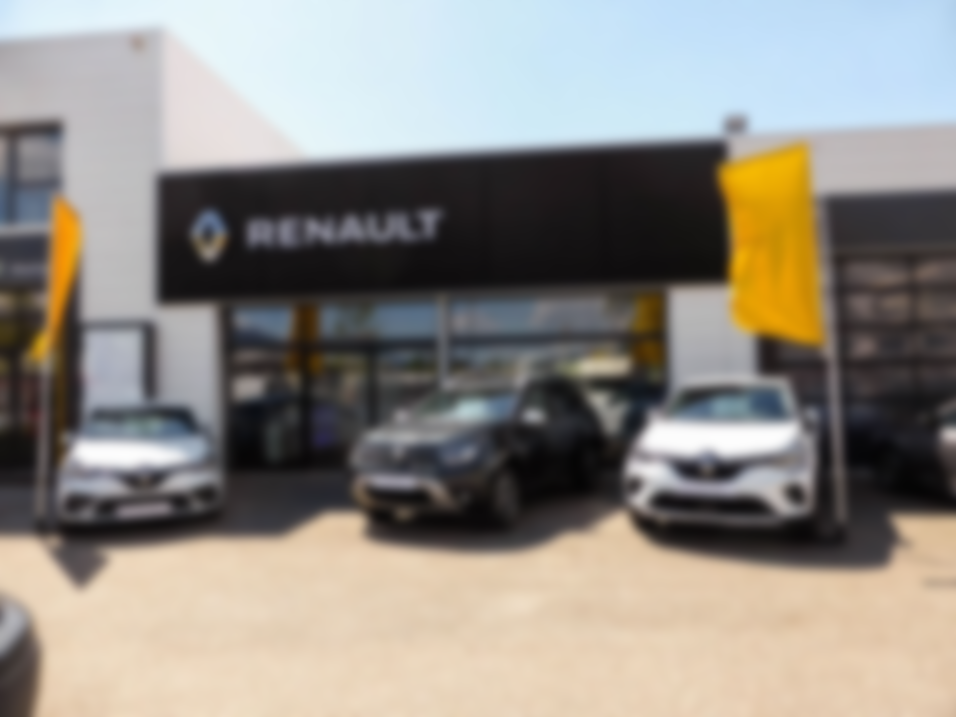 Une concession automobile Renault avec des voitures blanches garées devant le bâtiment. Un panneau indique 'RENAULT' en lettres blanches sur fond noir.