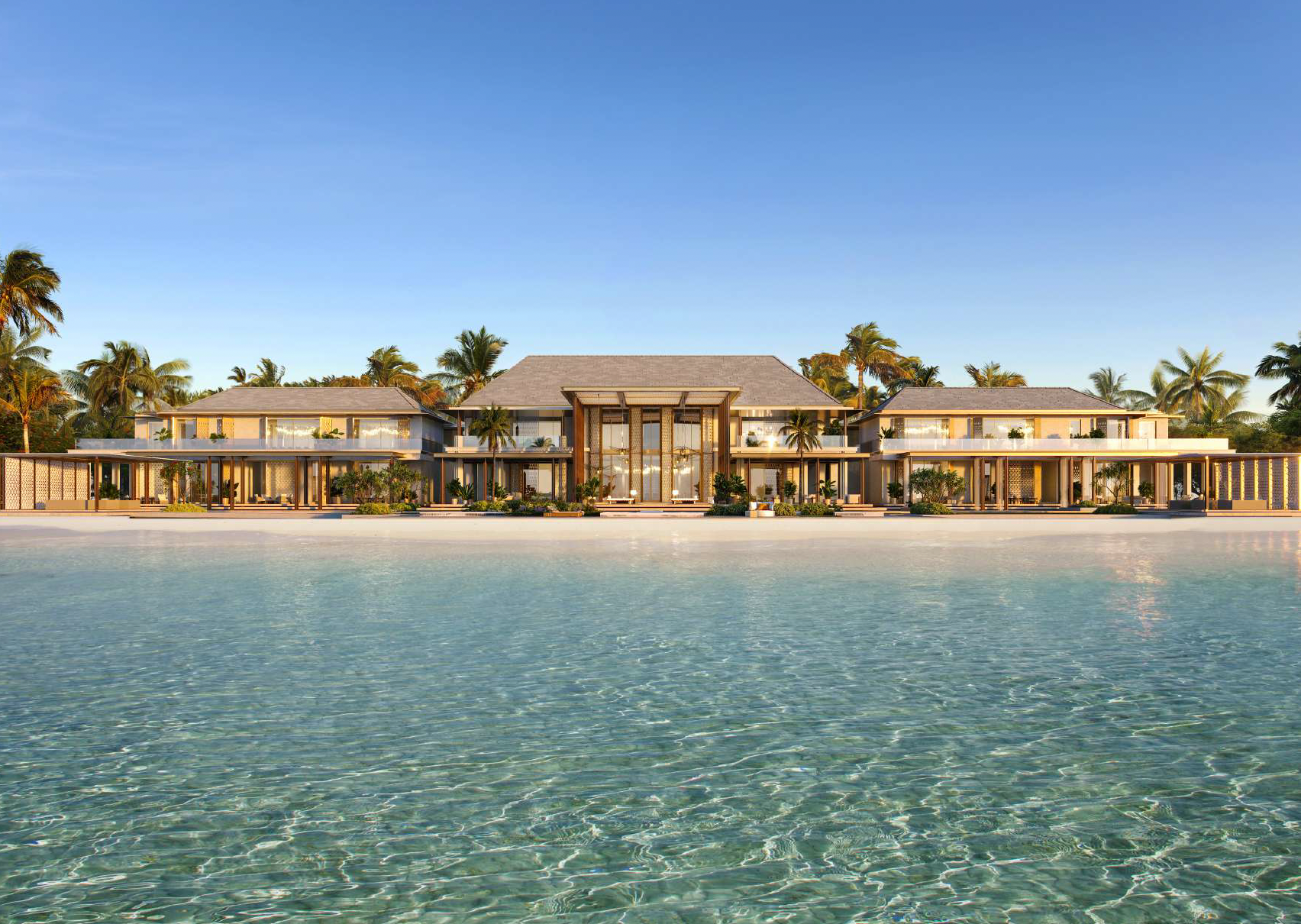 A luxurious modern beachfront house with large glass windows, surrounded by tall palm trees, with a calm water body in the foreground and a clear blue sky above.