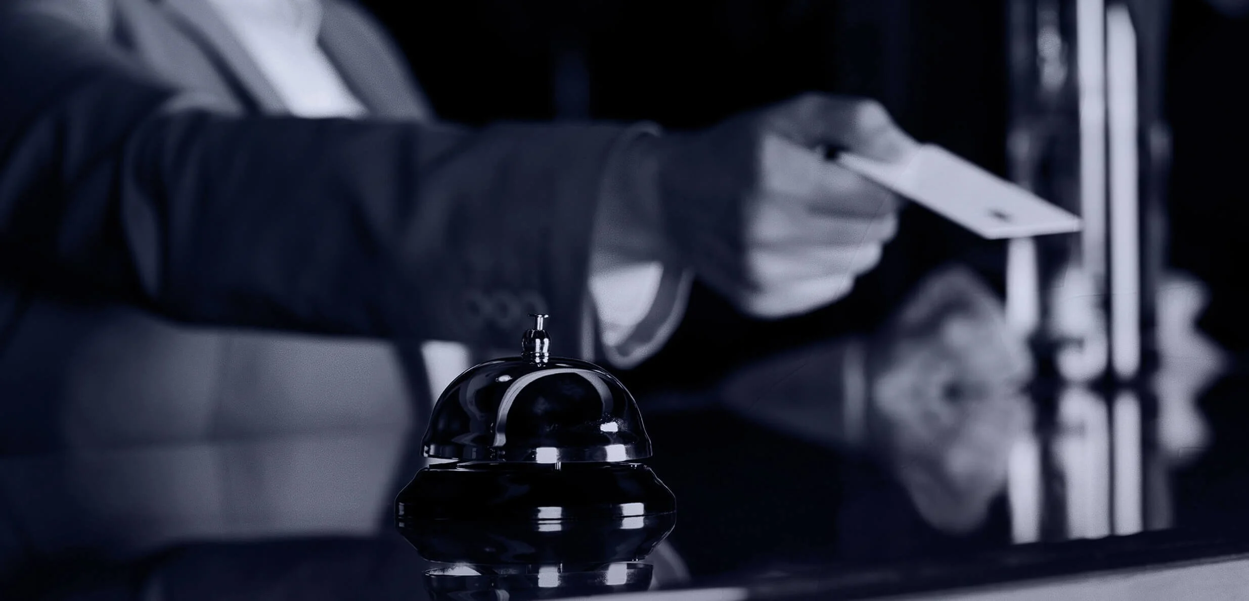 A person in a suit setting an alarm bell on a reflective surface, with a dark background.