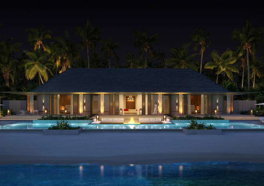 Night view of a luxury resort with a covered outdoor lounge area, swimming pools, and palm trees in the background.