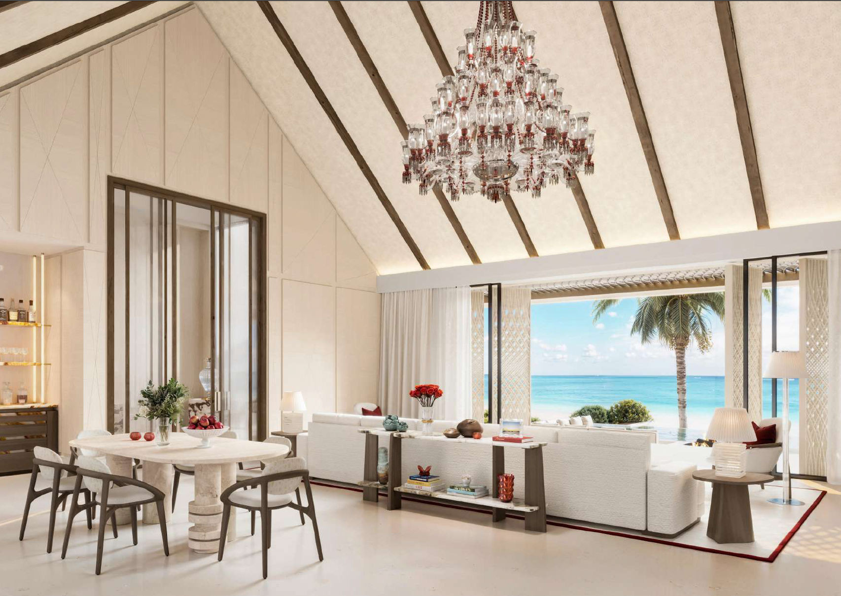 Spacious living room with a view of the beach and ocean through open sliding glass doors, featuring a high ceiling with wooden beams, a chandelier, white sofas, a round dining table with chairs, and tropical decor.