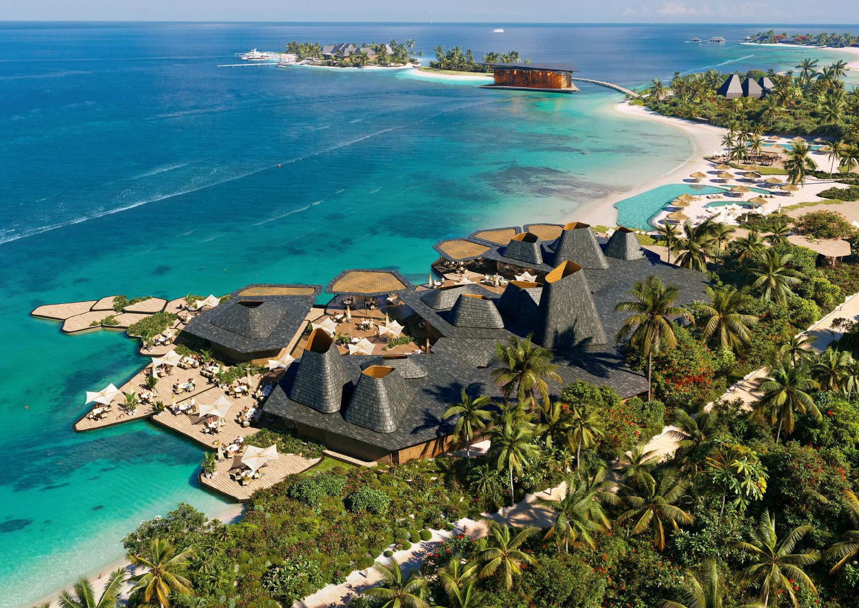 Aerial view of a tropical resort featuring multiple thatched-roof buildings, a large swimming pool, palm trees, and white sandy beaches with turquoise water, all overlooking the ocean.