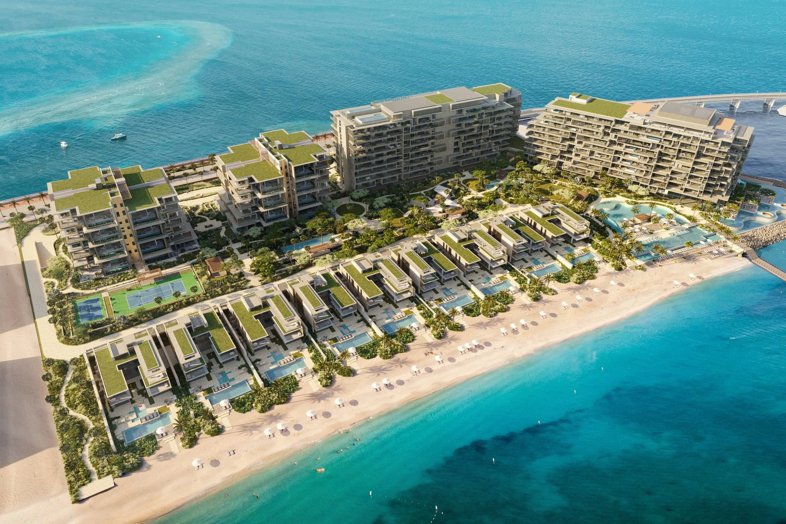 Aerial view of modern beachfront resort with multiple pools, greenery, and overwater bungalows by turquoise ocean.