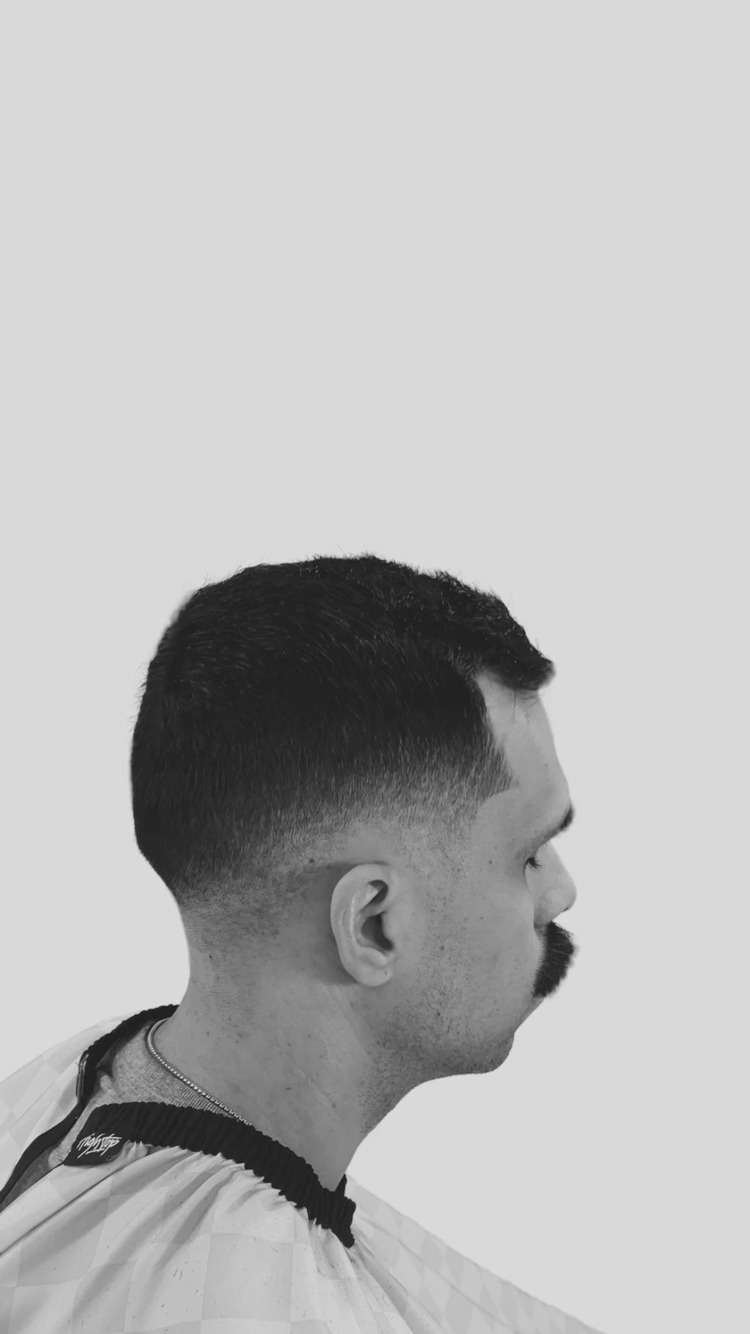 Side profile of a man with a textured fade haircut and a beard, wearing a barber cape.