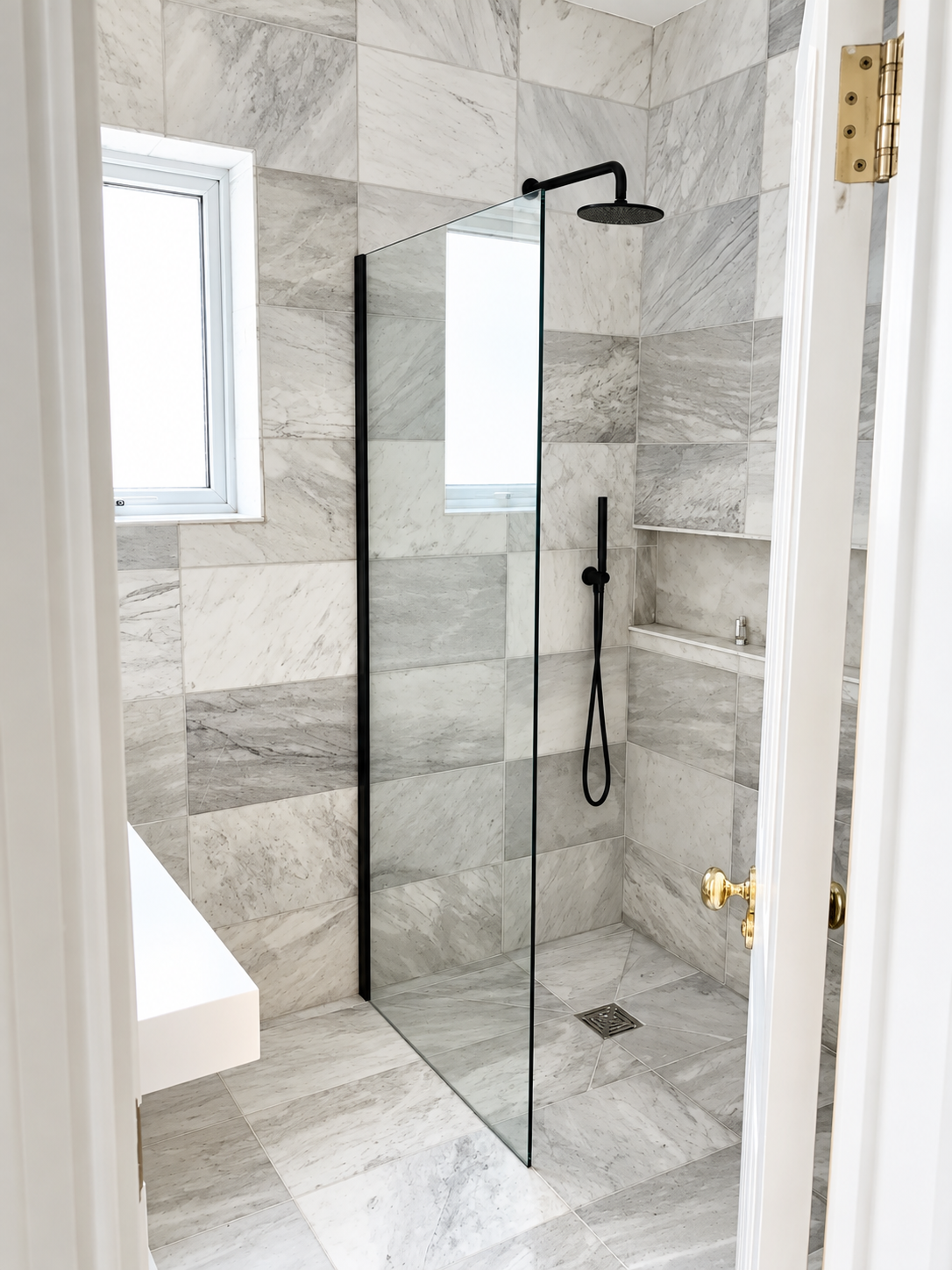 A luxurious walk-in shower featuring elegant marble-effect tiles, sleek matte black fixtures, and a frameless glass screen, creating a bright, modern, spa-inspired bathroom.