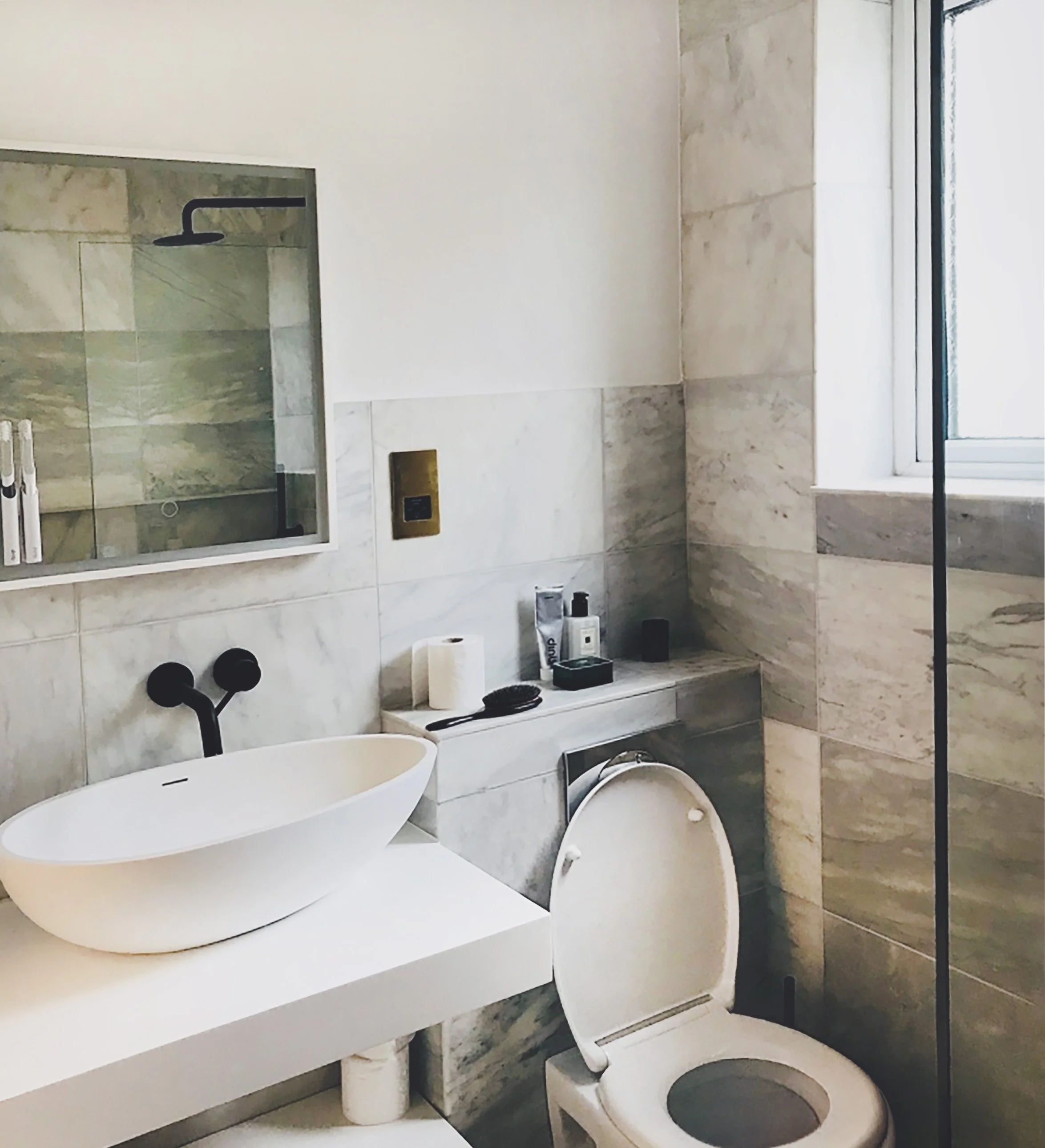Modern bathroom with marble walls, a white freestanding sink, a mirror, a toilet, and toiletries on the shelf