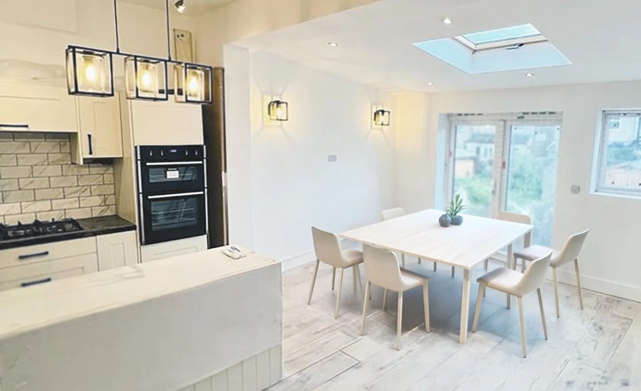 A bright, modern kitchen and dining area with a table and chairs, large windows, skylight, and contemporary light fixtures.