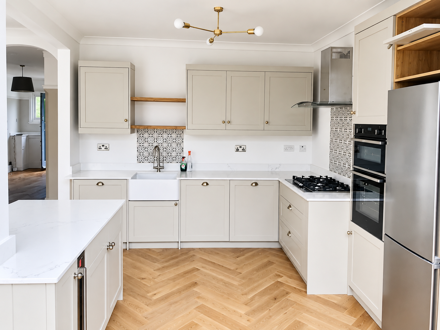 A beautifully designed contemporary kitchen featuring elegant shaker-style cabinetry, marble-effect worktops, warm brass accents, and stunning herringbone wood flooring for a timeless, sophisticated finish.