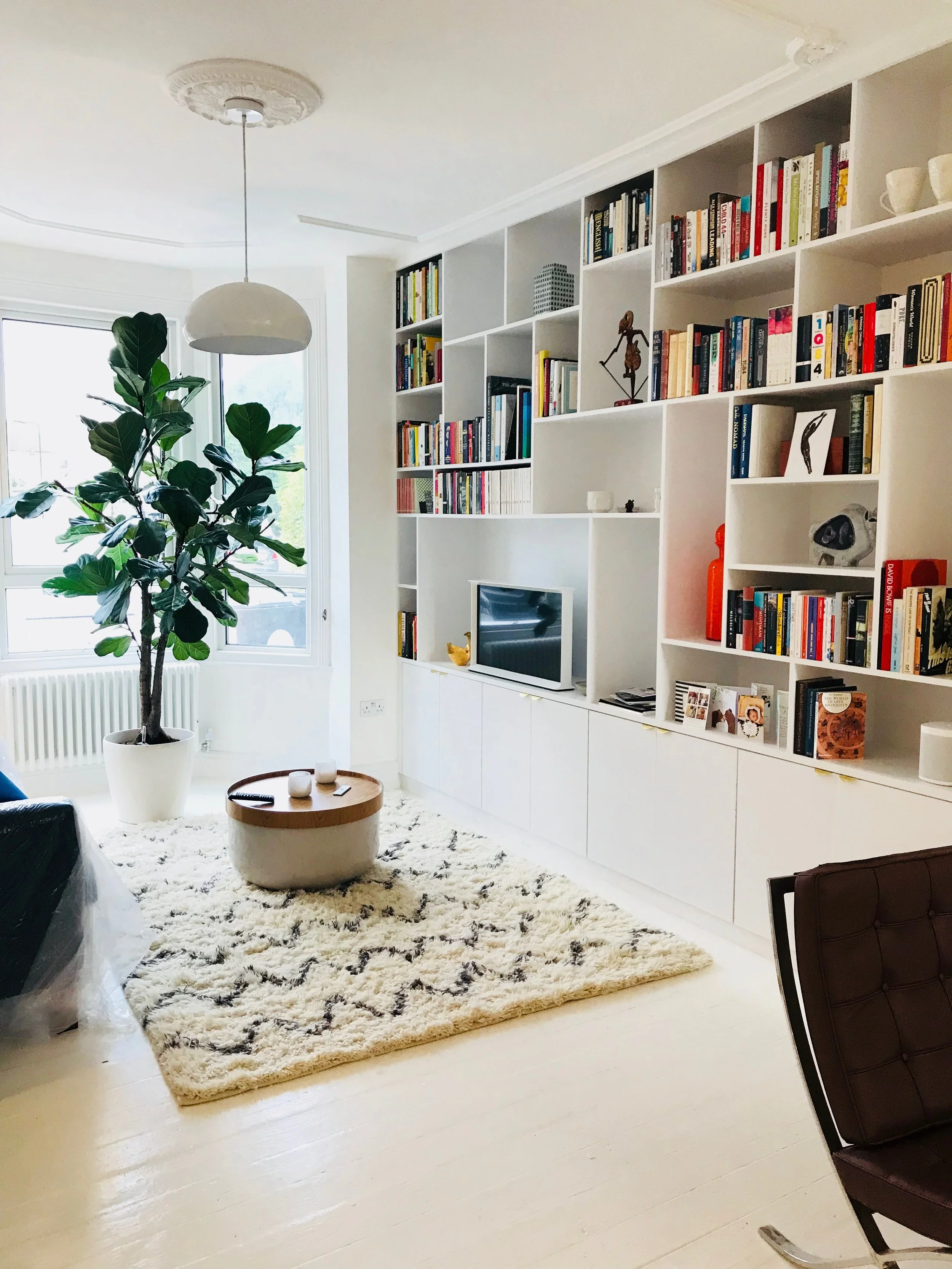 Modern living room renovation featuring bespoke floor-to-ceiling white bookshelves, integrated storage, a contemporary fireplace and bright, minimalist interior design in Hampshire.