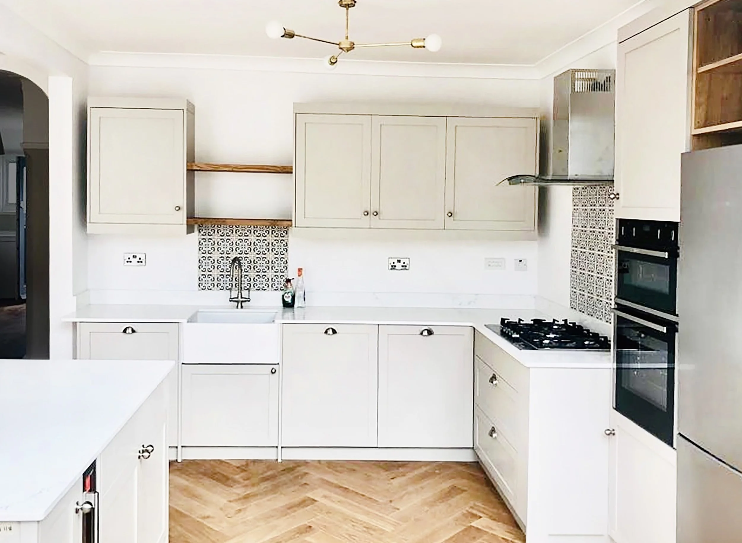View of a modern kitchen with white cabinets, a black oven, a gas stove, tiled backsplash, and a wooden floor.