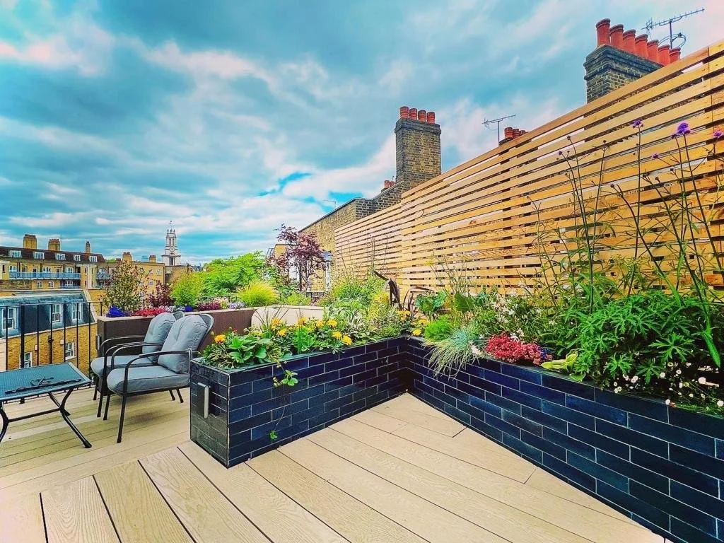 Modern rooftop terrace featuring timber decking, bespoke raised brick planters, lush landscaping, contemporary outdoor seating and timber privacy screening in Surrey.