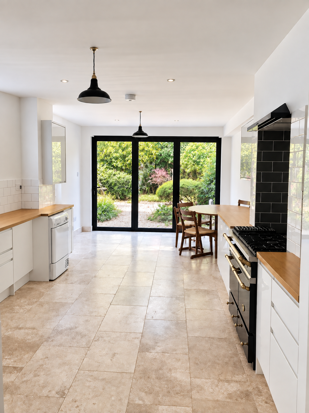 A bright, contemporary kitchen featuring sleek white cabinetry, warm wooden worktops, bold black accents, and elegant tiled flooring, with a cosy dining area overlooking a lush garden.