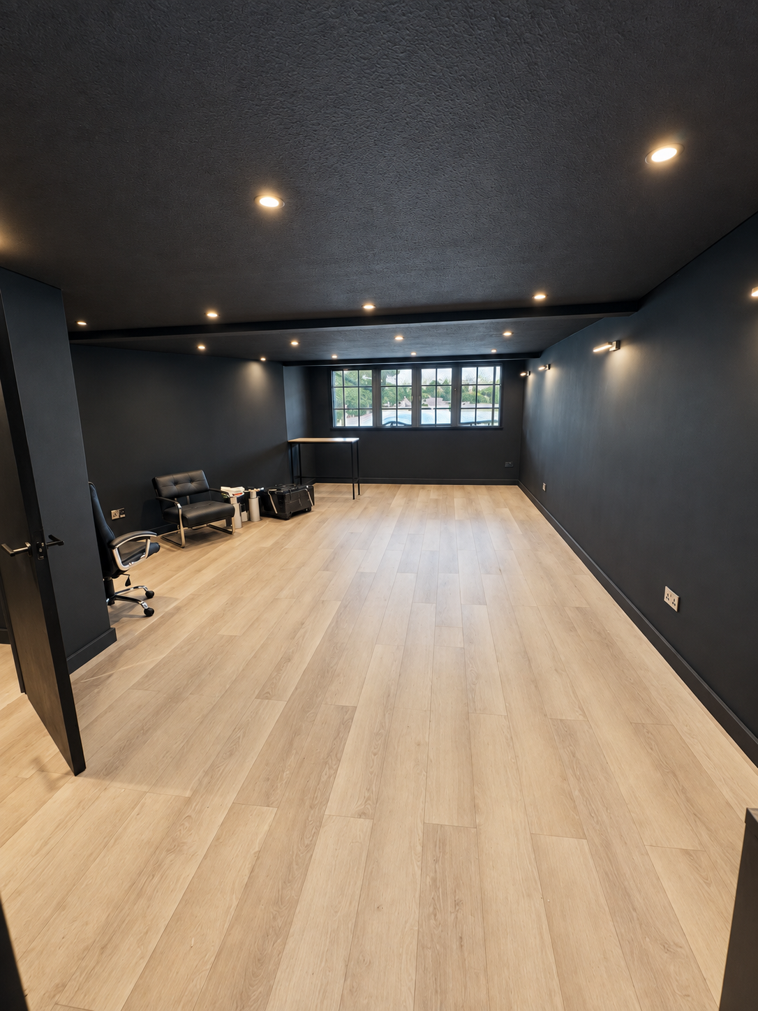 Modern commercial interior refurbishment featuring dark charcoal walls, recessed ceiling spotlights, light oak-effect flooring and a spacious open-plan layout. 