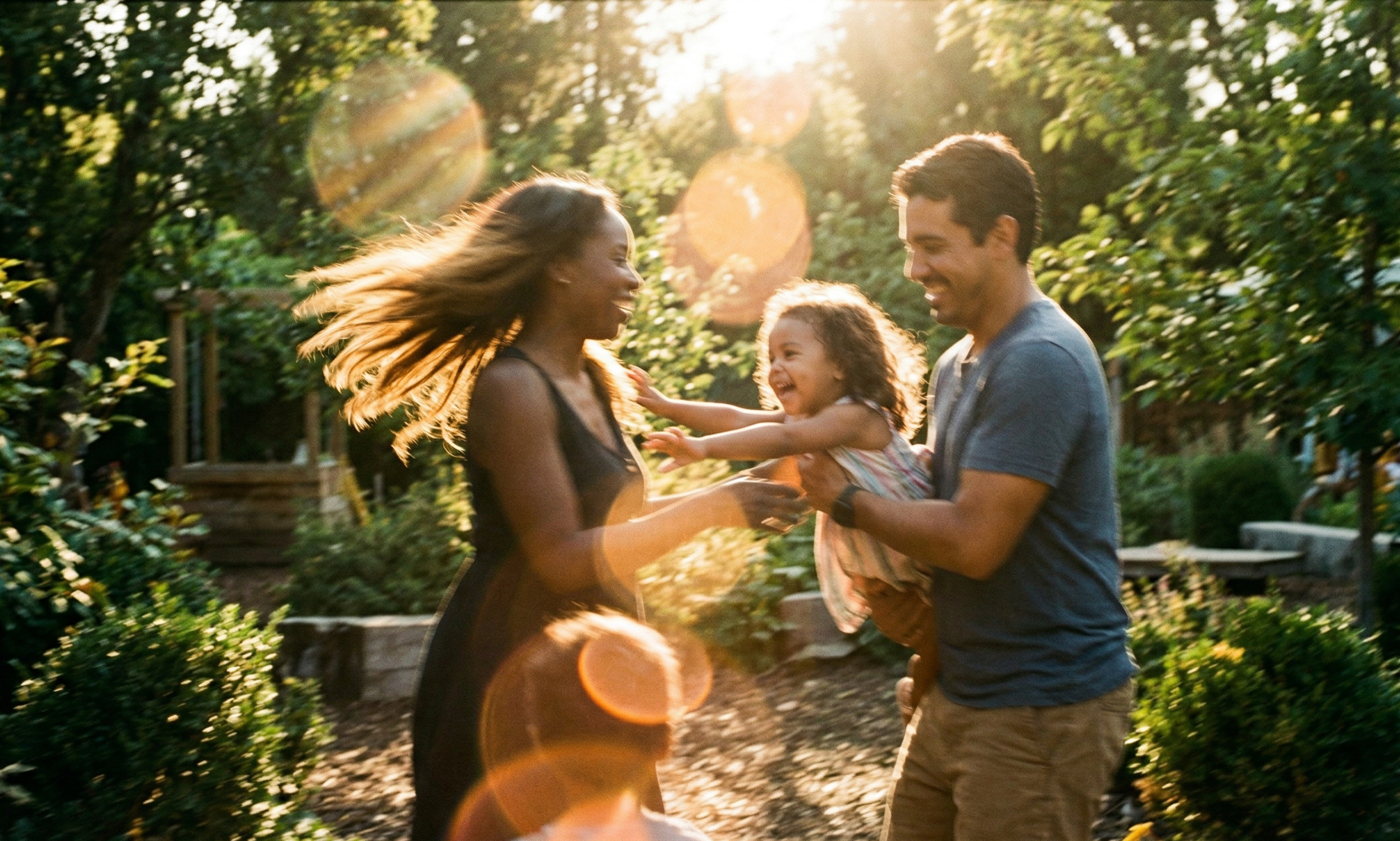 An interracial, international family enjoying a playful moment outdoors in the sunlight, showing the greeneries of Switzerland. It epitomises what The Orangerie Club manifests; the premium family club that is for both children and parents to grow.