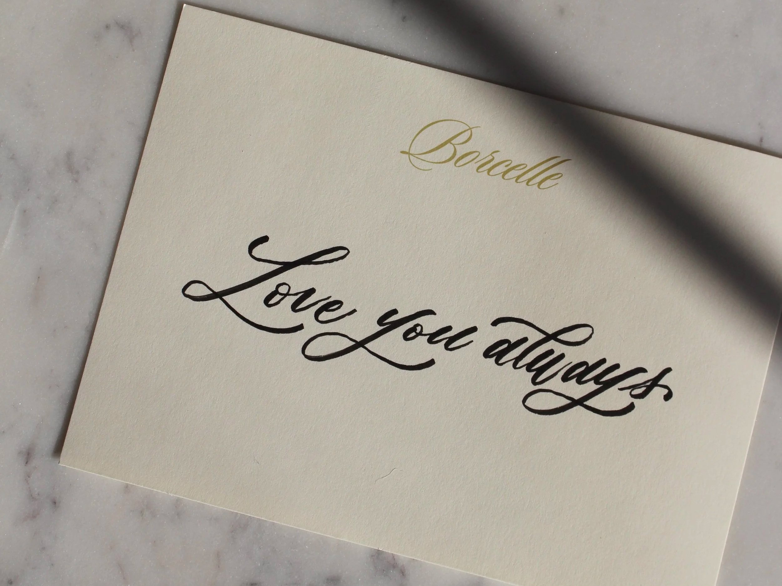 A gift message on an ivory card sits in the sunlight and reads "Love you always"