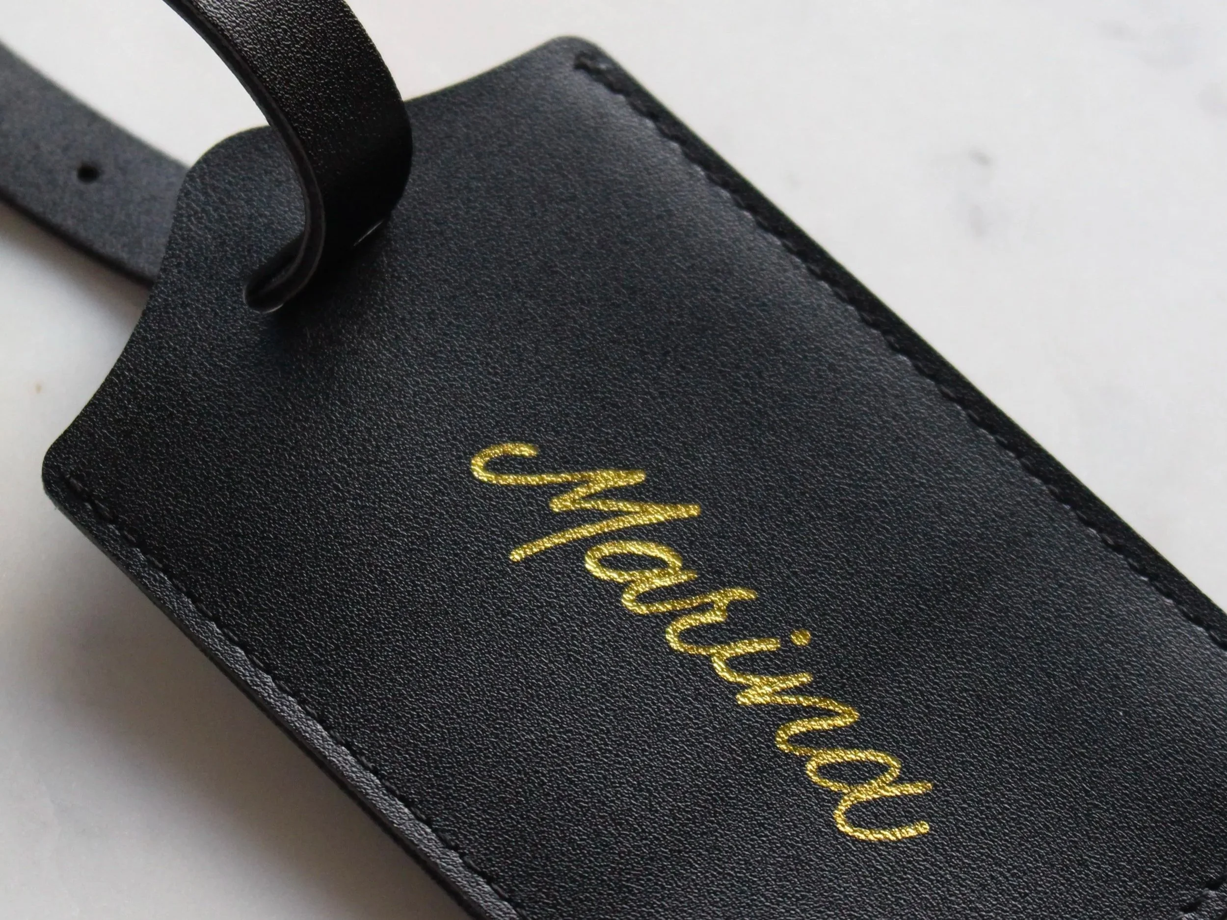 A closeup of a black leather luggage tag sits with the name "Marina" on it