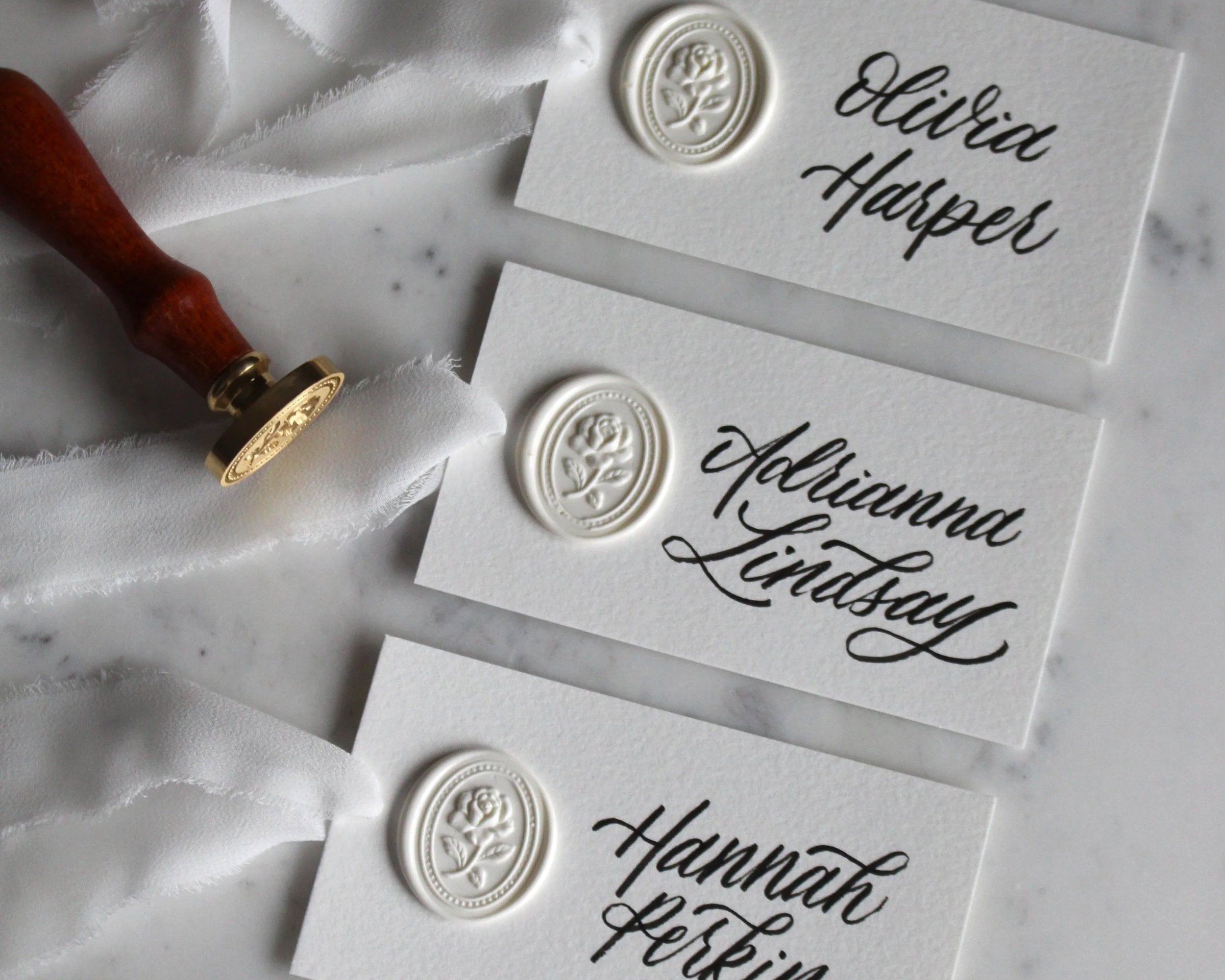 Elegant, white, calligraphy place cards with ribbon, handwritten names and wax seals.