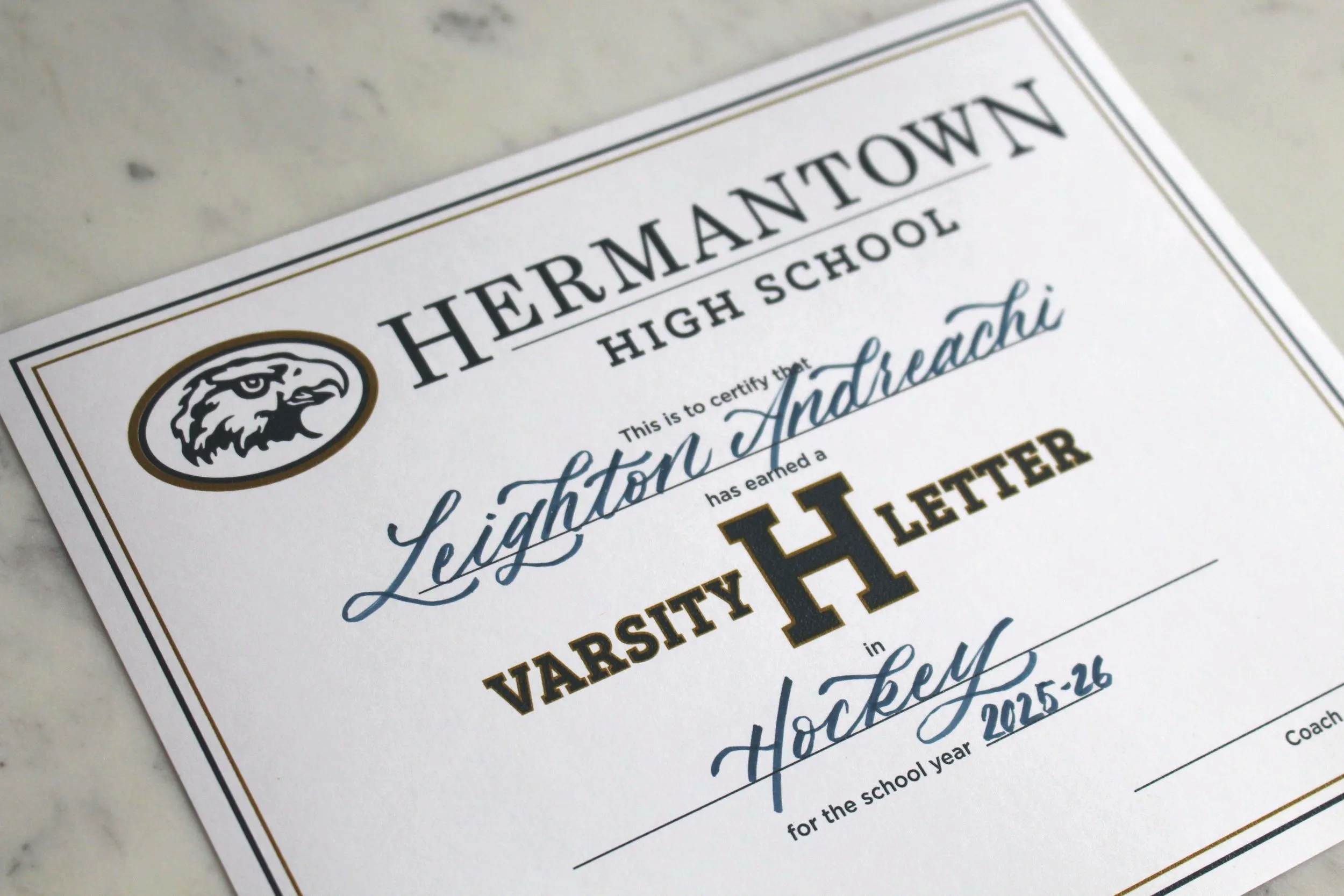Image shows a Hermantown varsity letter with the name "Leighton Andreachi" who lettered in Hockey during the 2025-26 School Year