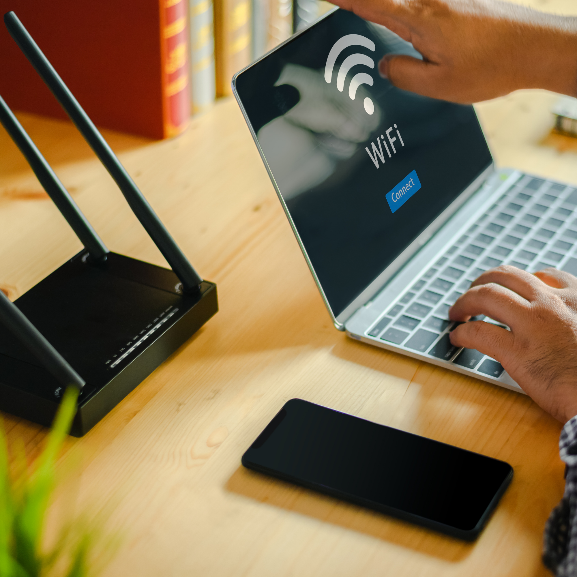 A person using a smartphone showing a Wi-Fi connection screen, placed on a wooden desk with a keyboard nearby and bookshelf in the background.